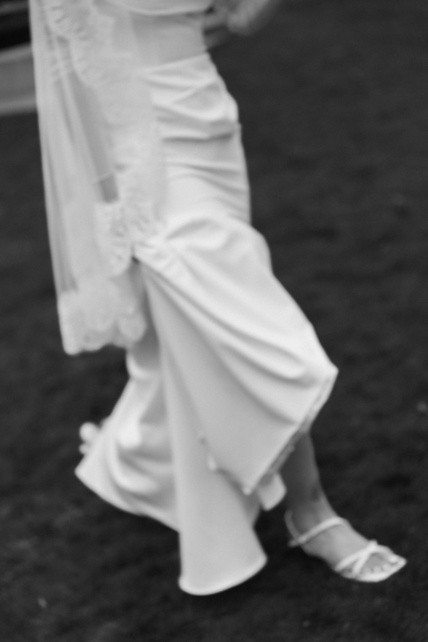 Black and white detail shot of bride's flowing white dress and elegant shoes.