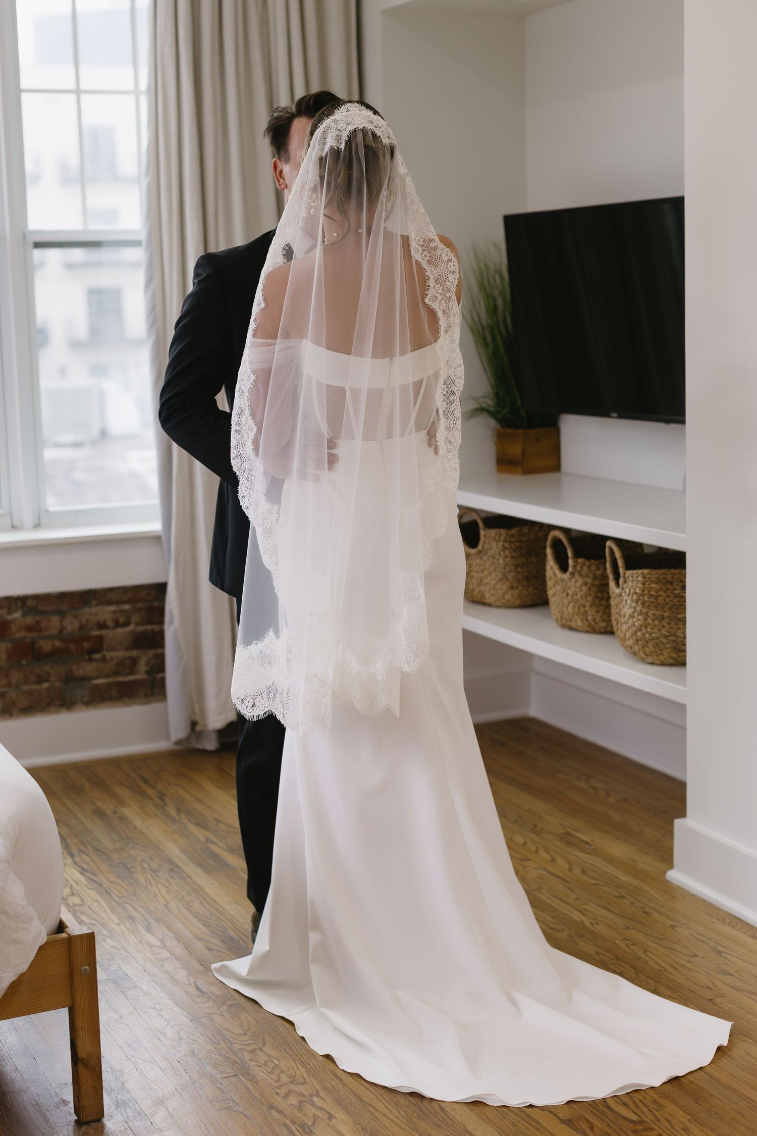 Wedding dress with flowing veil being fitted in a modern room with hardwood floors.