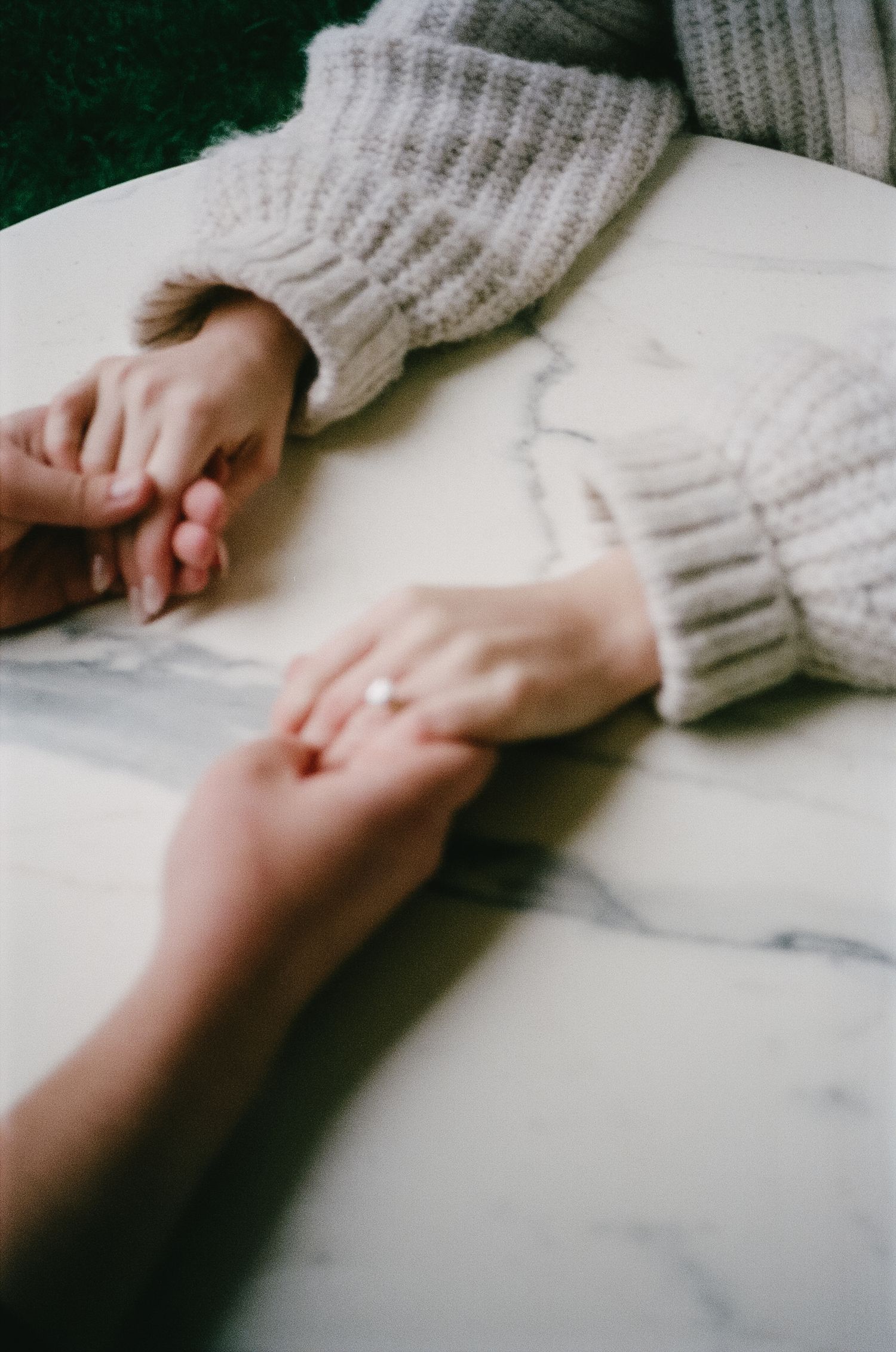 Close-up of hands gently touching on white marble surface wearing cozy knit sweater sleeves.