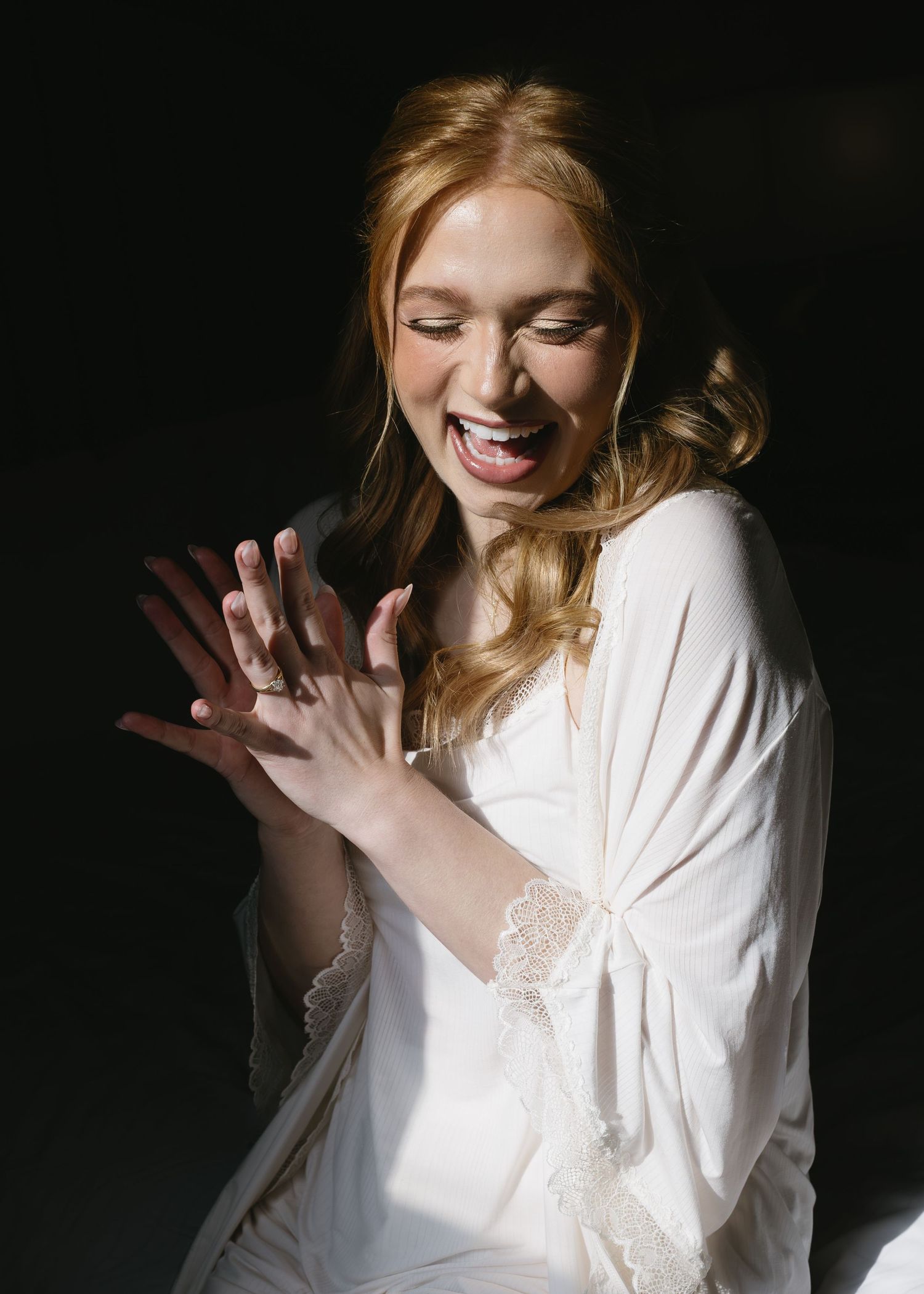 Candid sequence showing joyful reactions and laughter in white lace robe against dark background.