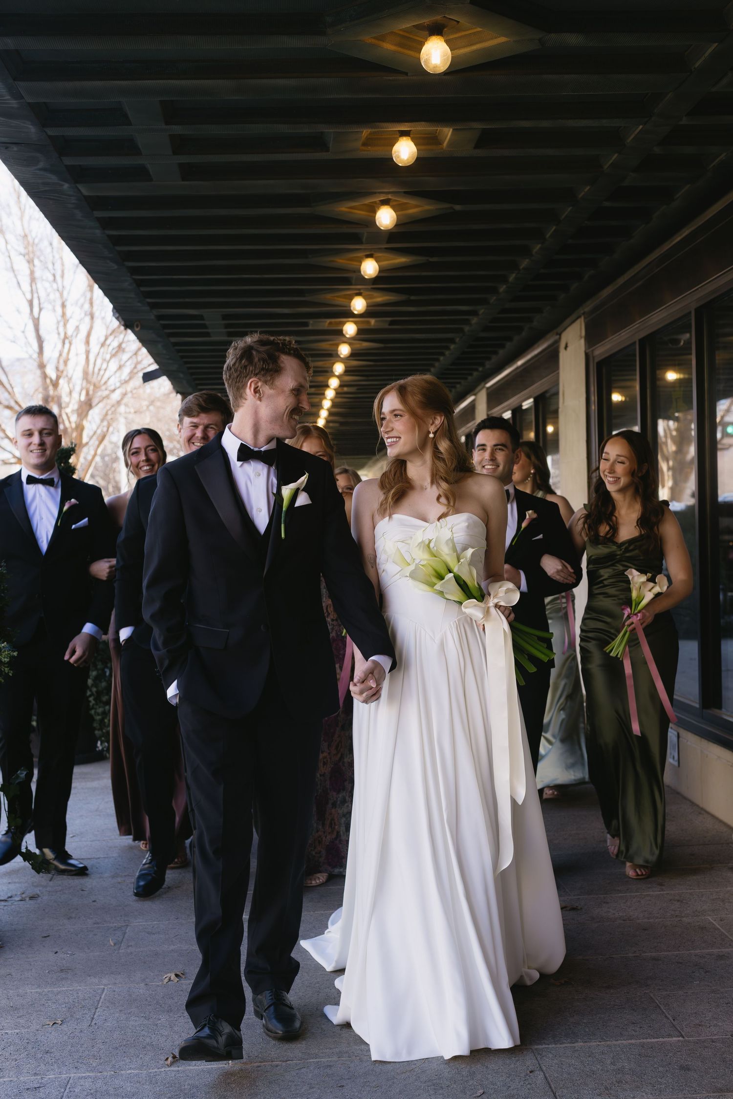 Wedding party gathered in a covered walkway with overhead lighting and industrial ceiling details.