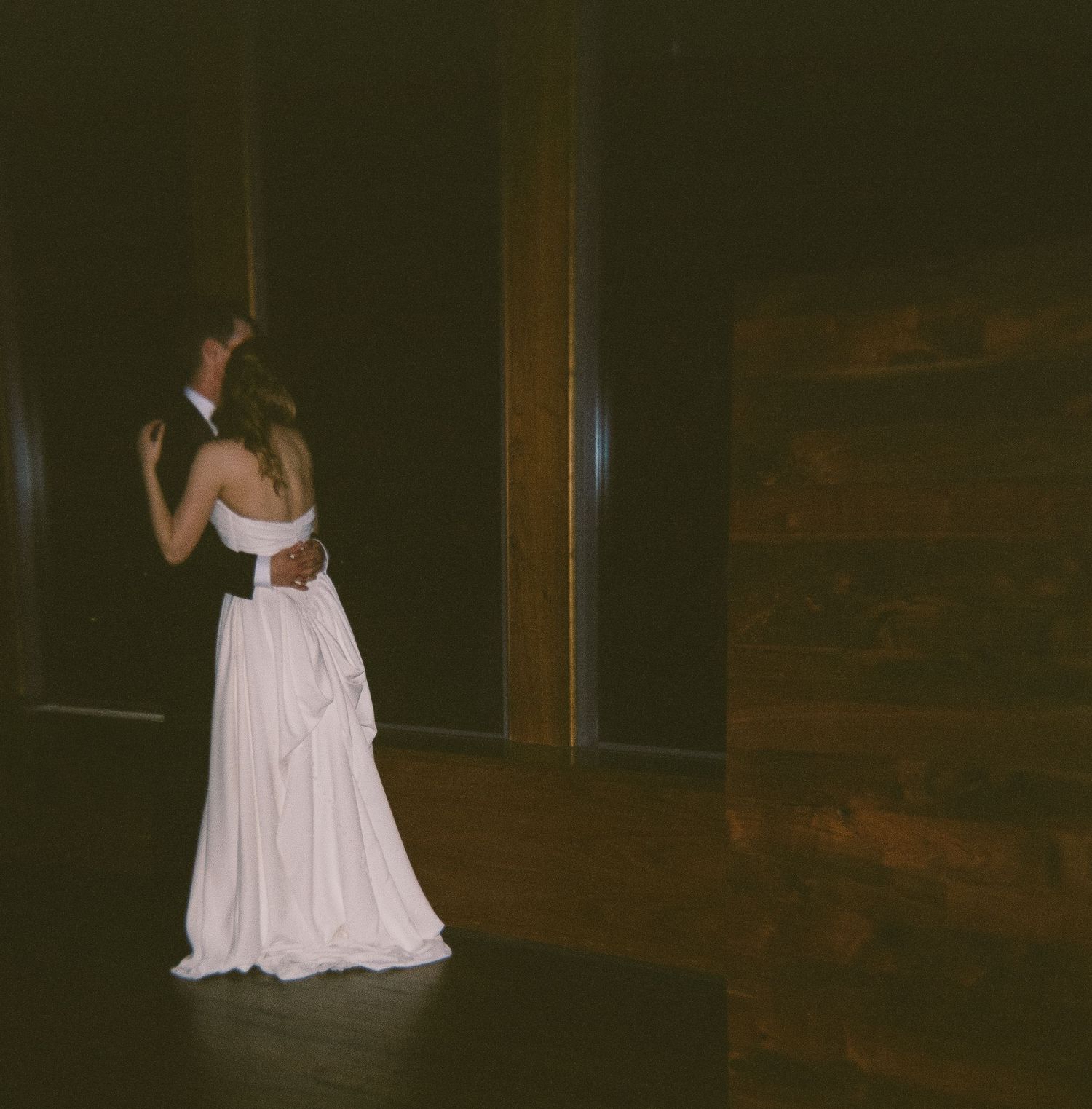 Wedding dance floor scene with a bride in white dress dancing in a dimly lit rustic venue.
