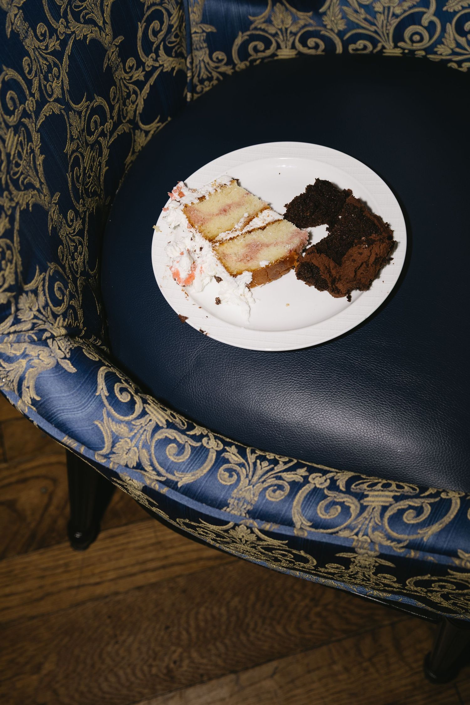 Plates of wedding cake on an ornate blue and gold patterned chair.
