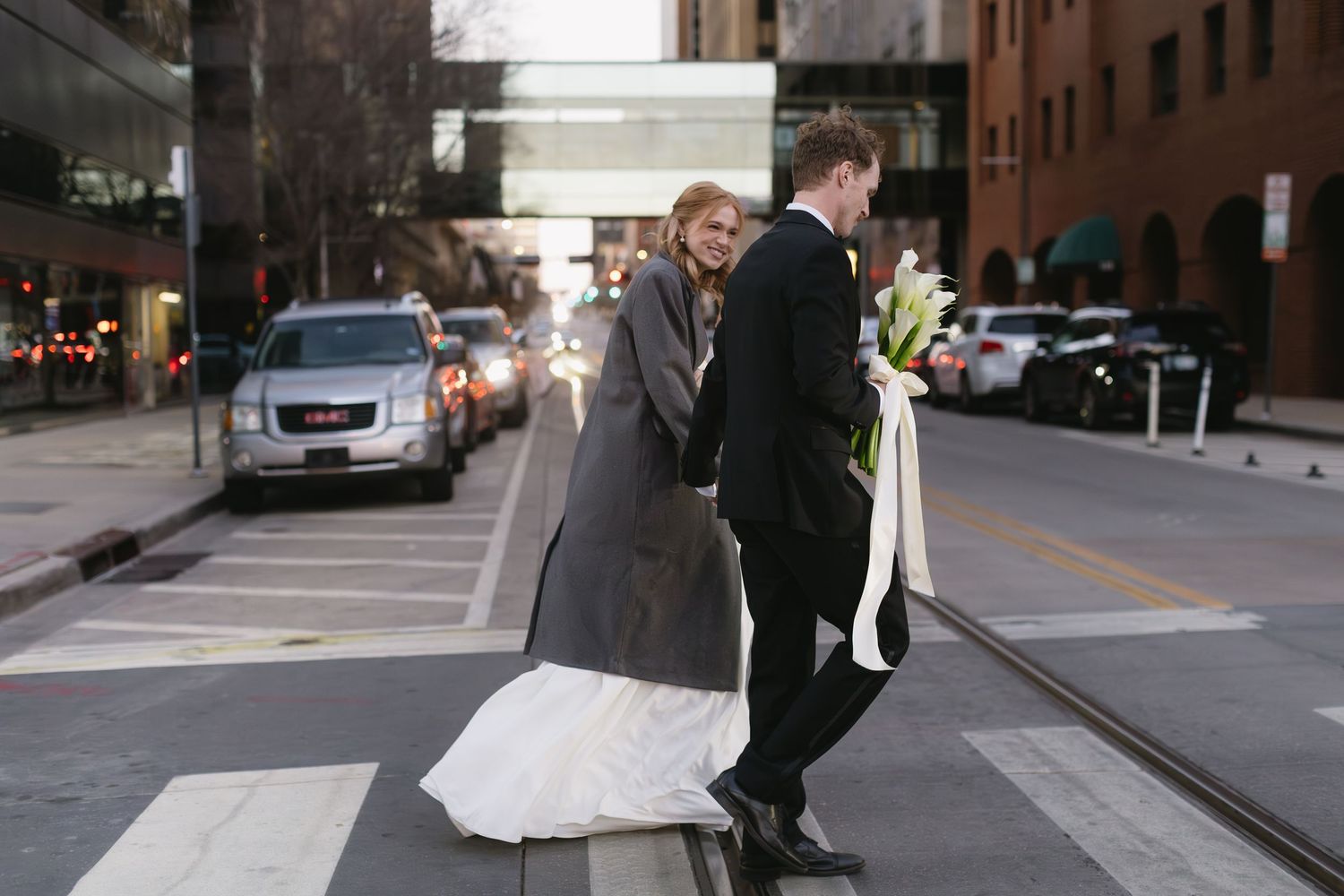 Wedding couple strolls down a city sidewalk holding hands.