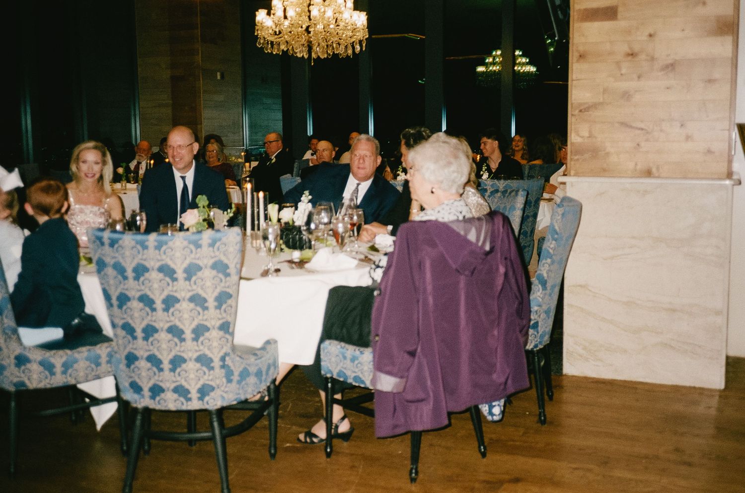 Wedding reception dinner setting with crystal chandelier and elegant table arrangements.