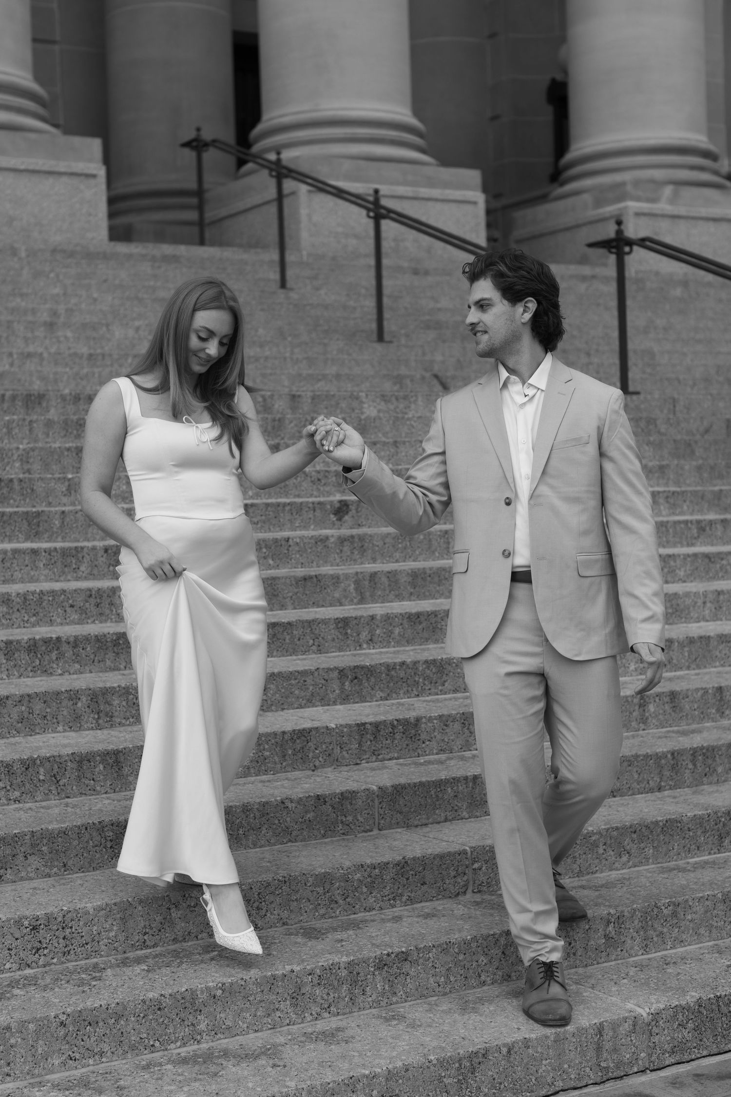 A couple in formal attire descends elegant stone steps in a black and white photograph.