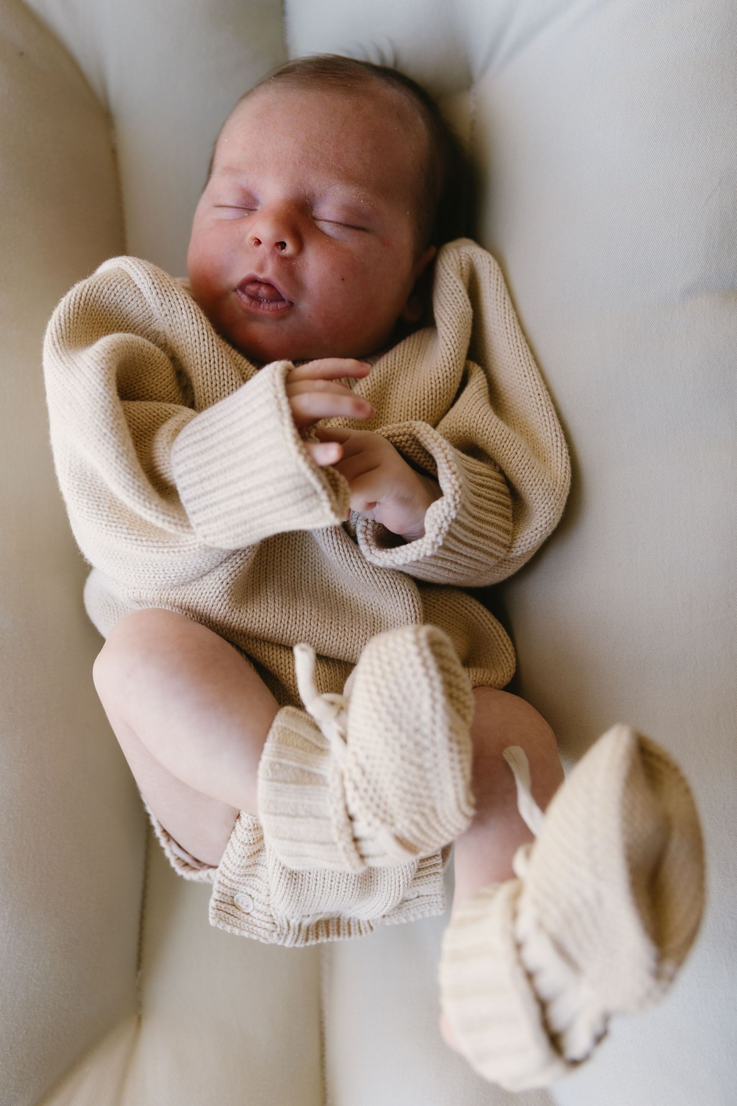 A peaceful sleeping newborn wrapped in a cozy cream-colored knit sweater rests on white bedding.
