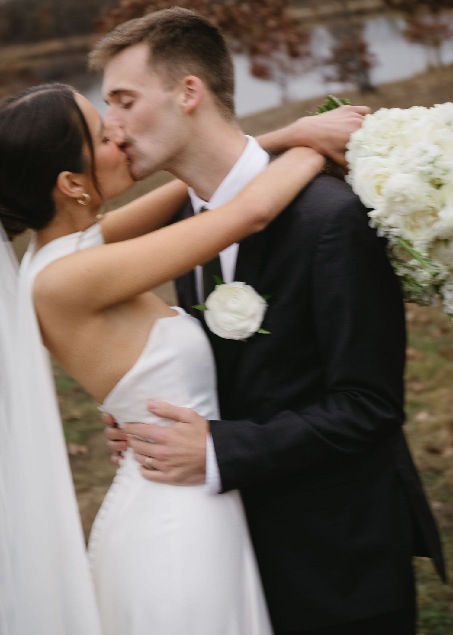 Romantic wedding couple embraces outdoors in autumn with white floral bouquet and flowing bridal veil.