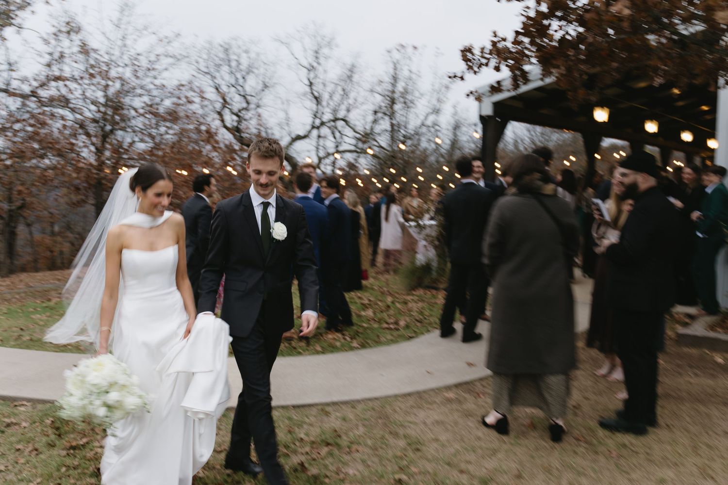 Wedding party stands outdoors on a fall day with bare trees in the background.