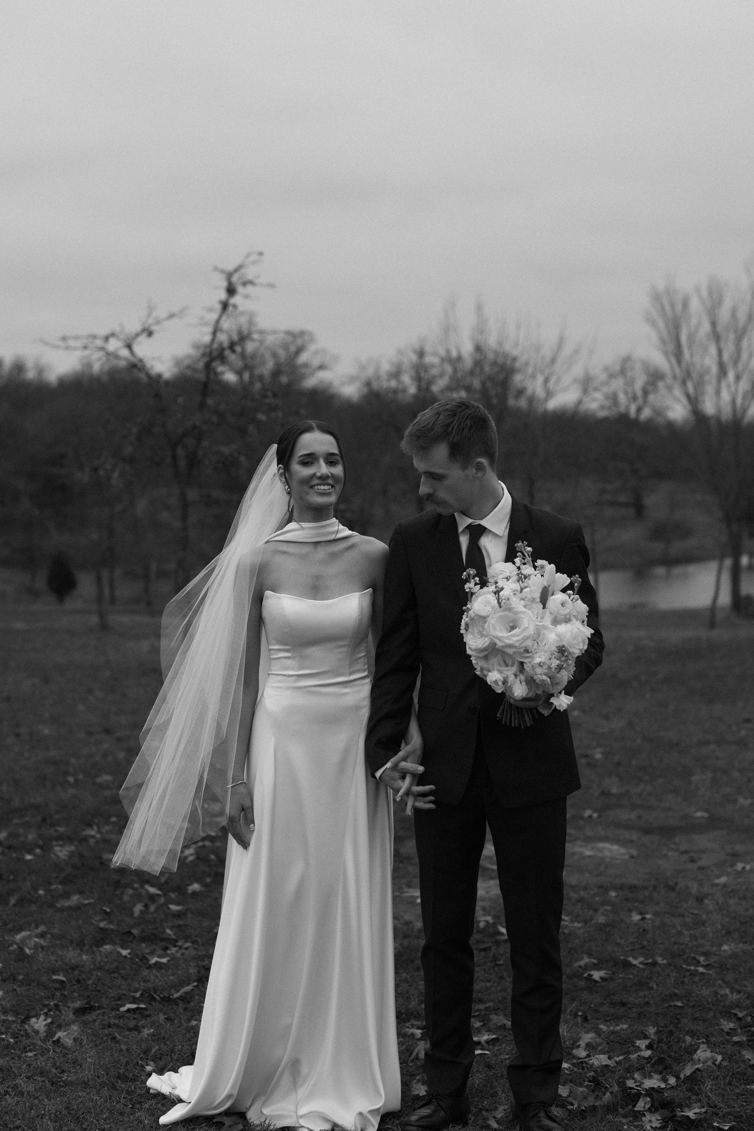 Black and white wedding photography in a scenic outdoor setting with bare trees.