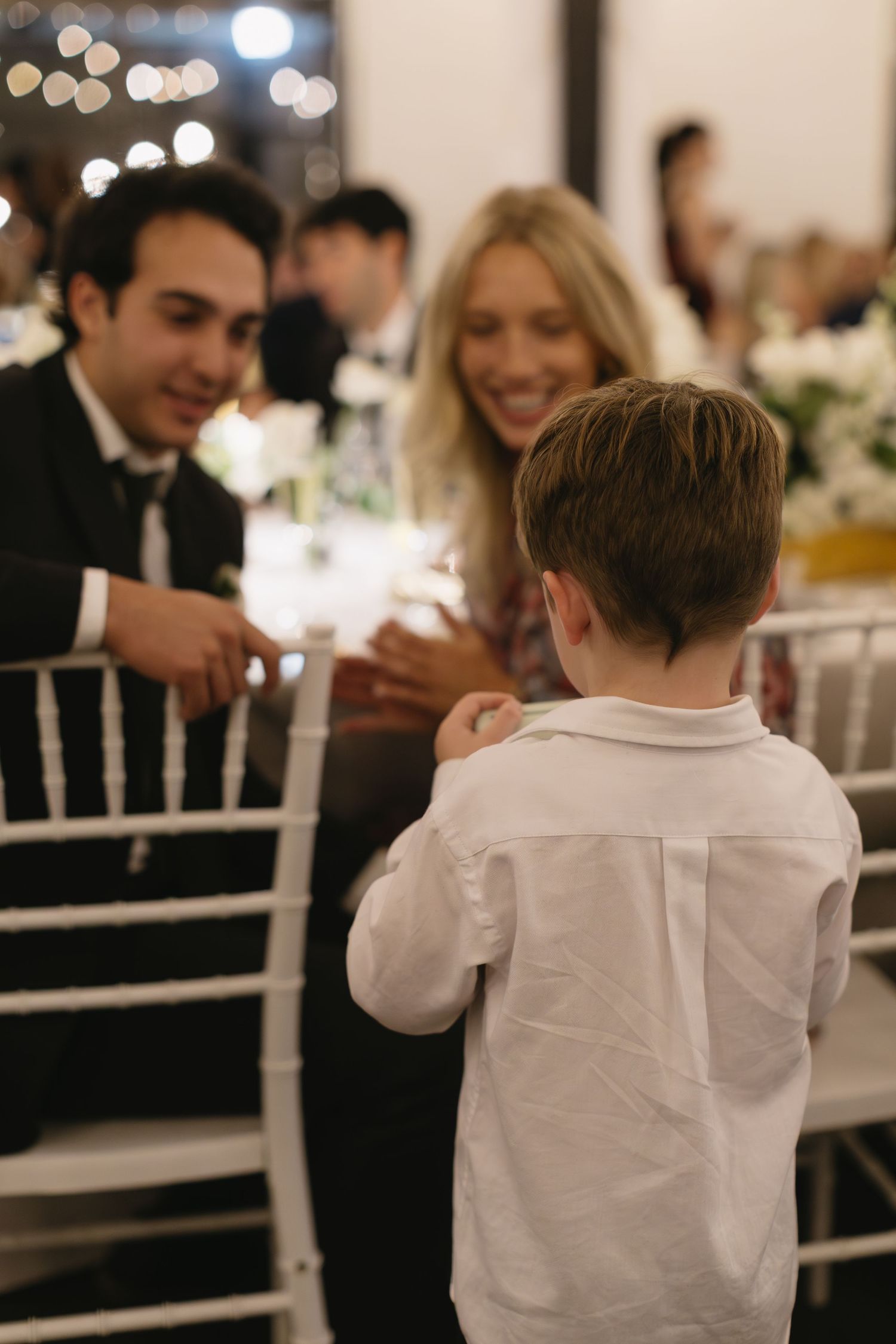 Wedding reception guests seated at tables with white linens and string lights overhead.