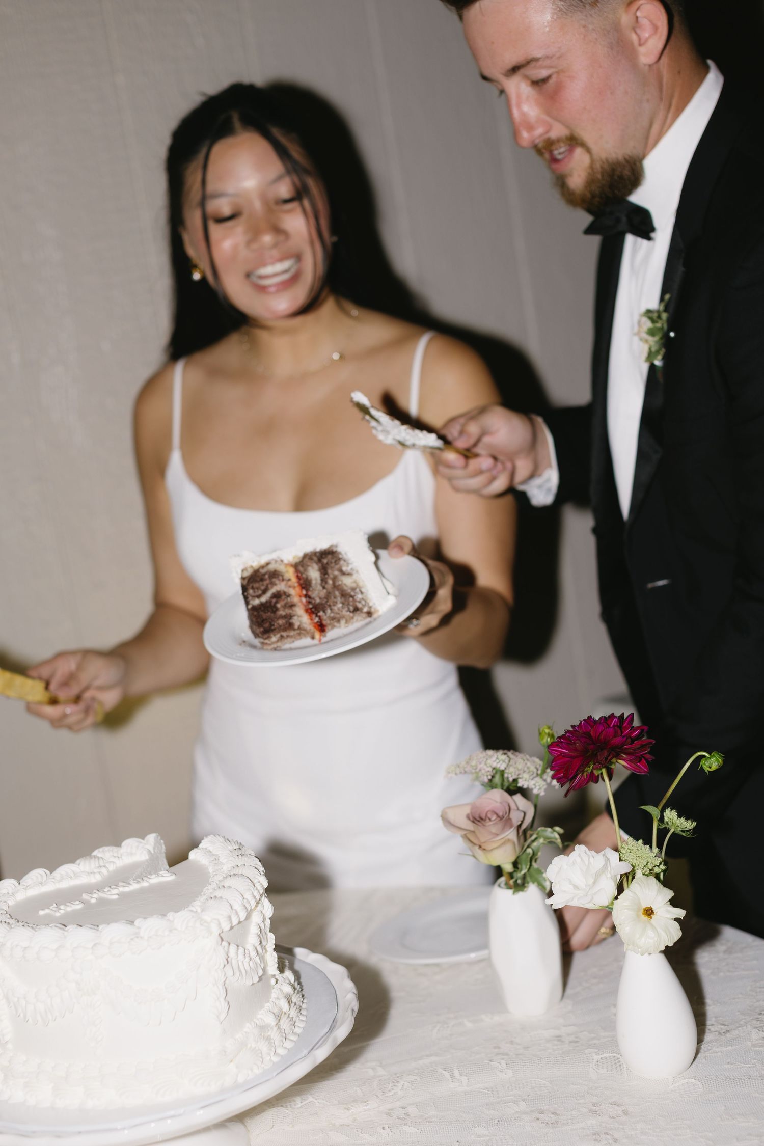 Bride and groom share cake cutting moment at wedding reception with white floral decorations.