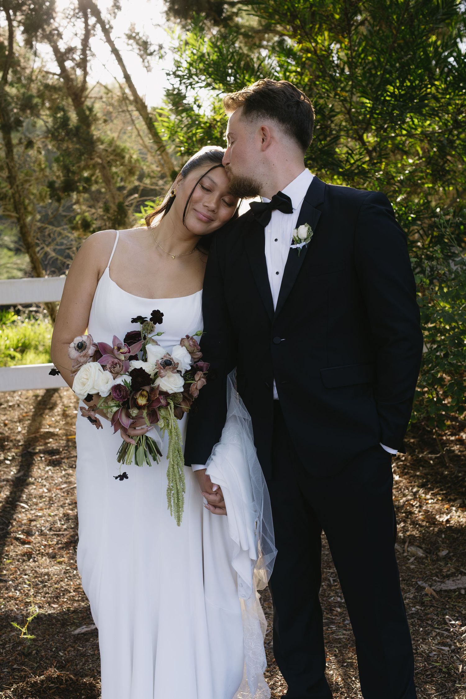 Romantic outdoor wedding portraits with couple holding bouquet against natural foliage.