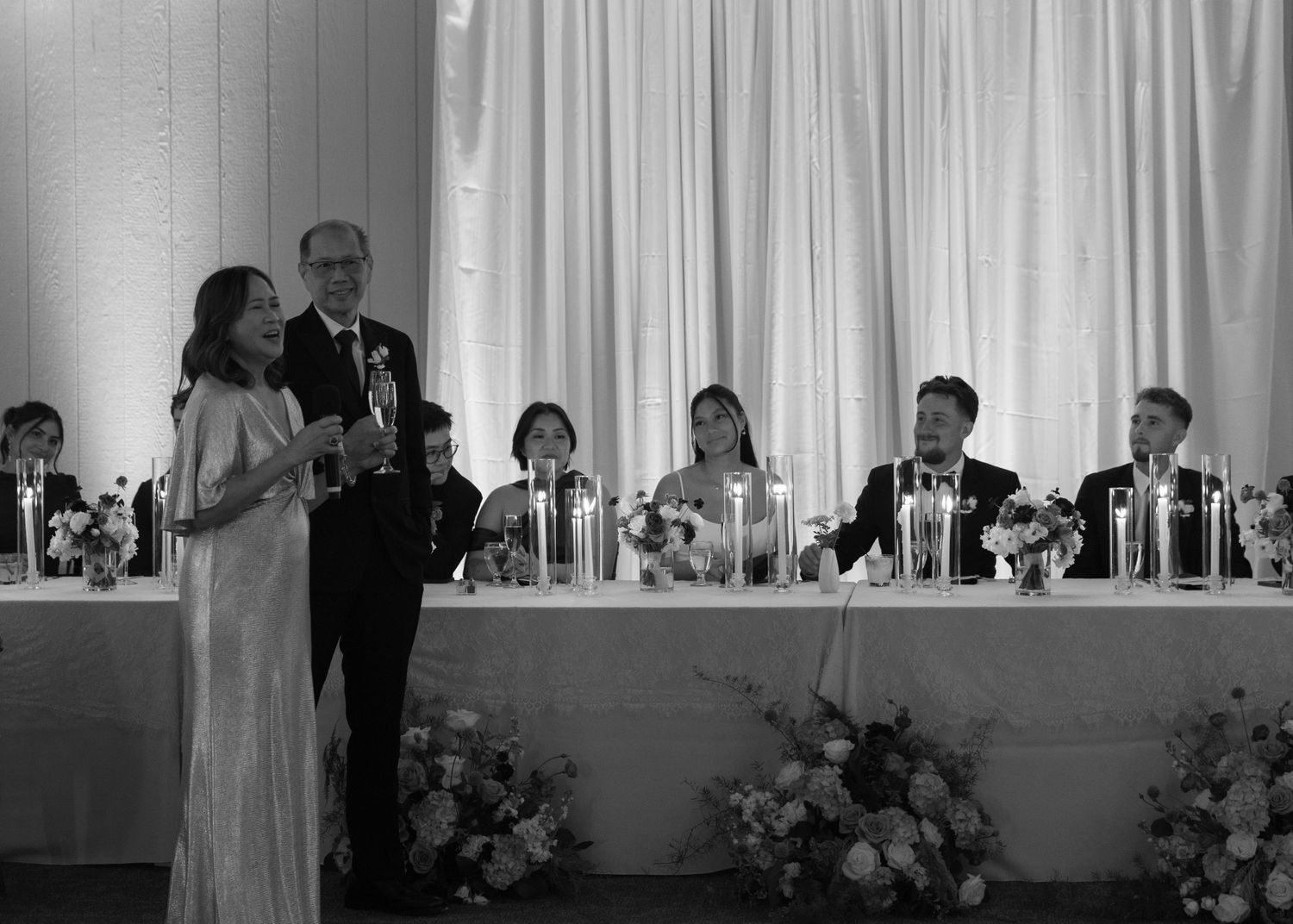 Wedding reception head table setup with white draping and floral arrangements.