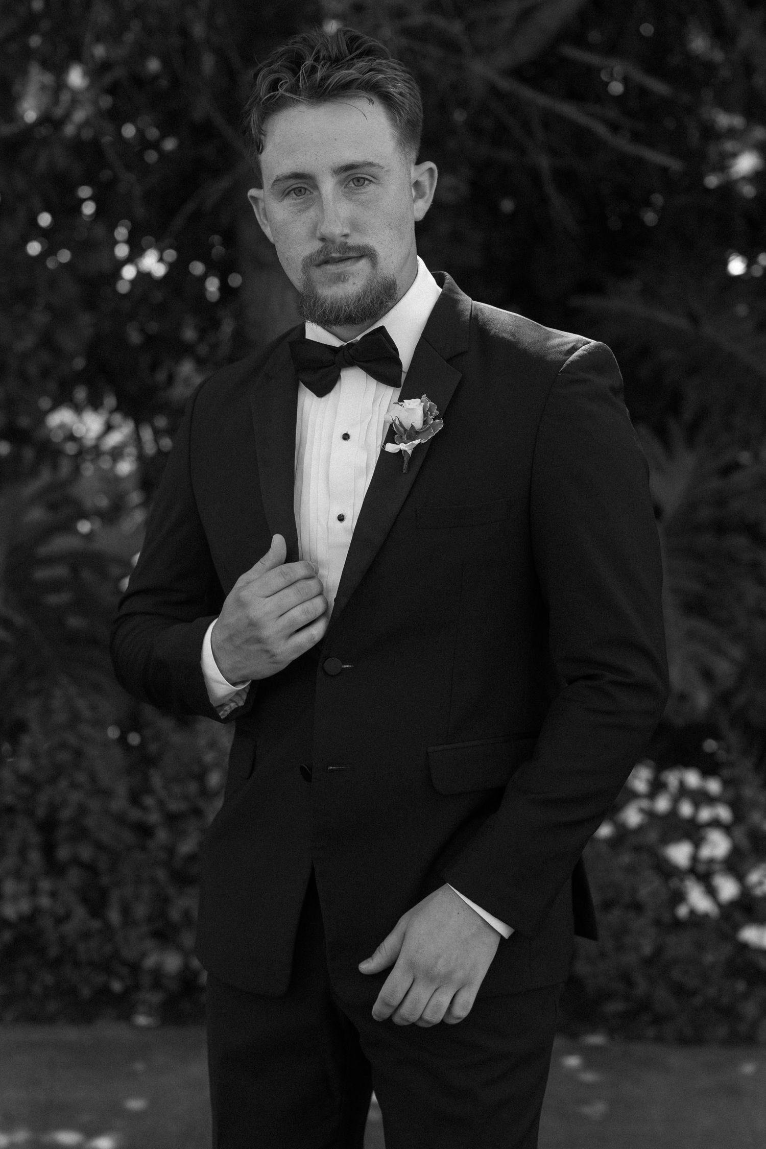 Close-up portrait shots of groom in classic black tuxedo and bow tie against natural background.