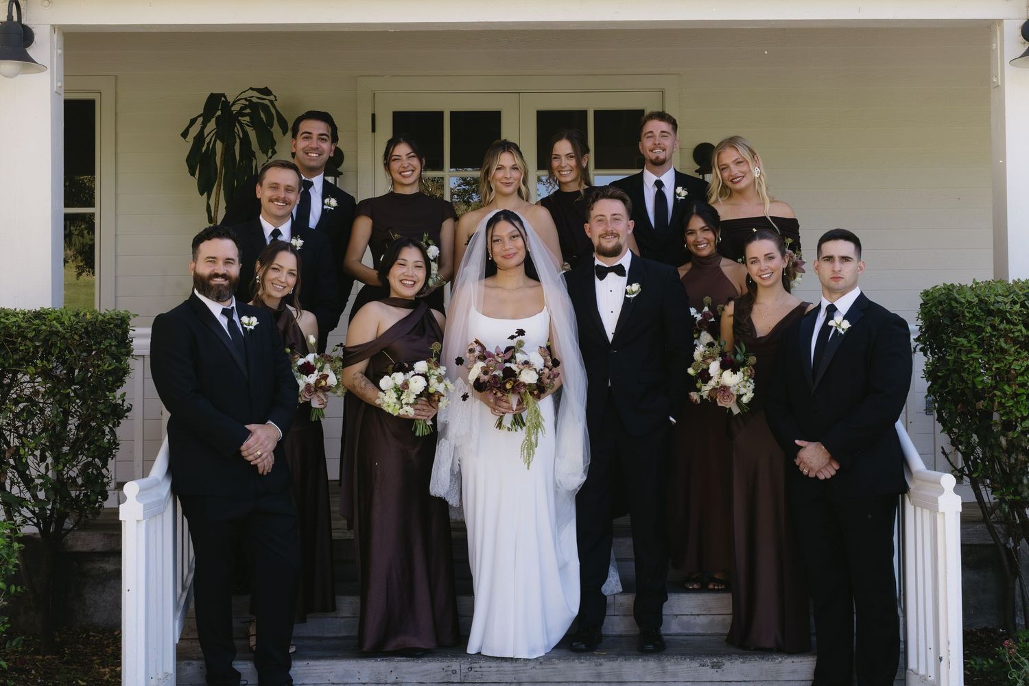 Wedding party poses together on a white porch for formal group photos.