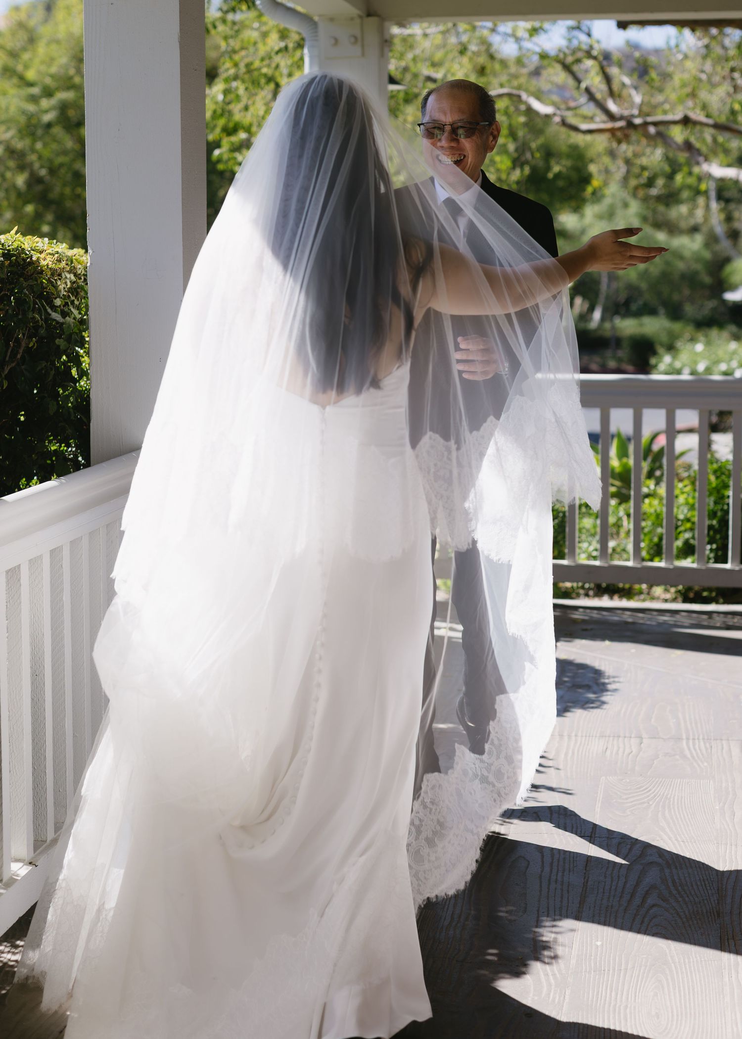 White wedding dress and veil flowing elegantly on an outdoor porch with garden views.