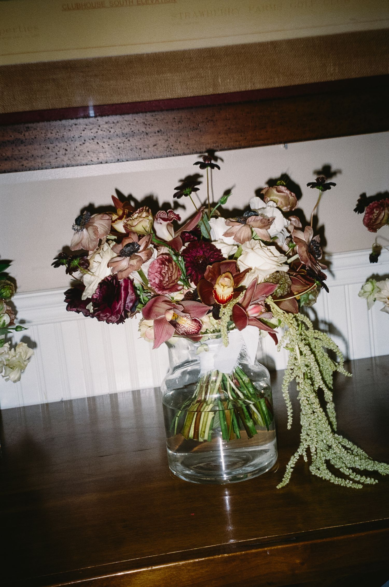 Row of glass vases filled with pink and burgundy floral arrangements on a dark wooden surface.