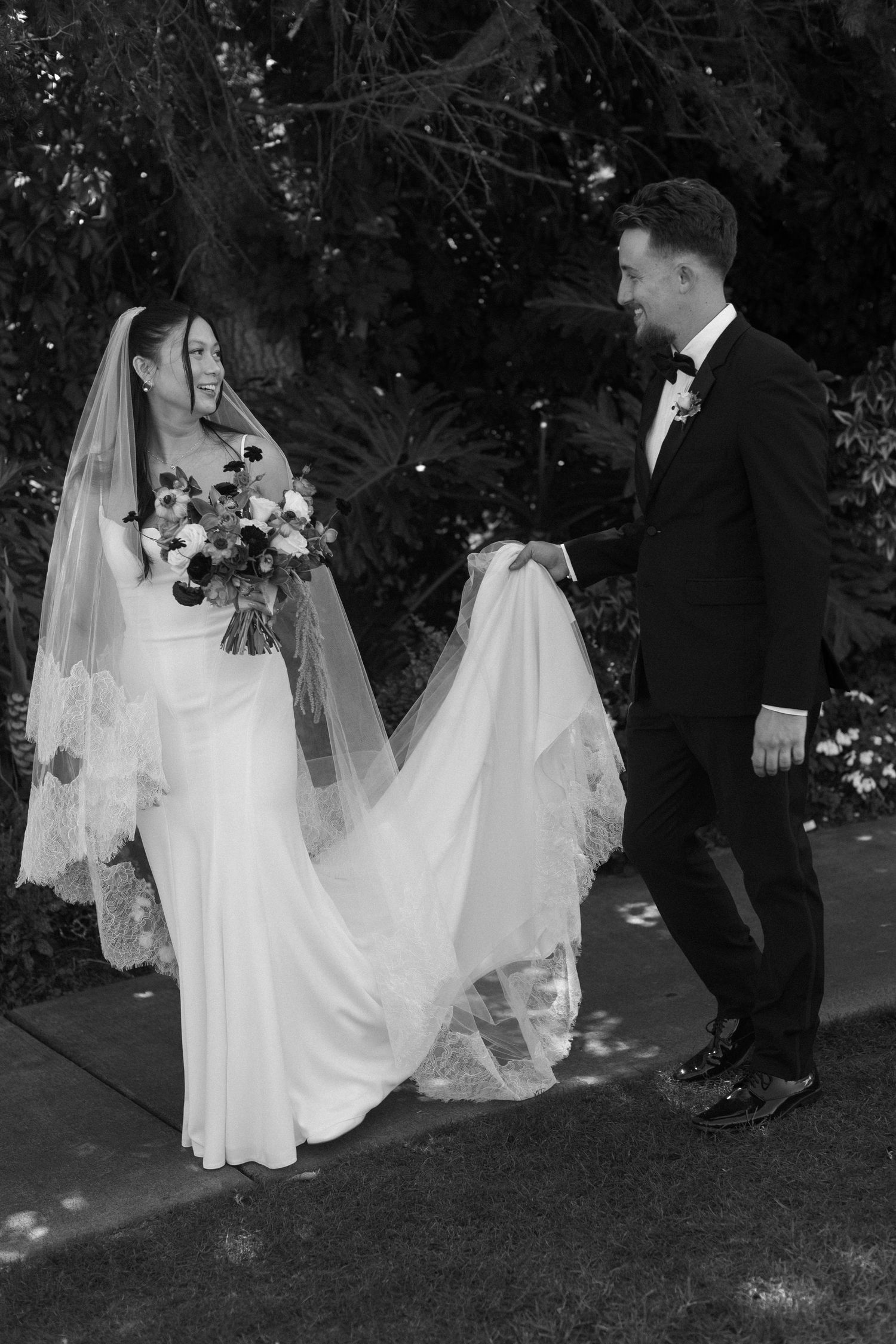 A bride's white dress trails behind her as she walks across grass with others in formal attire.