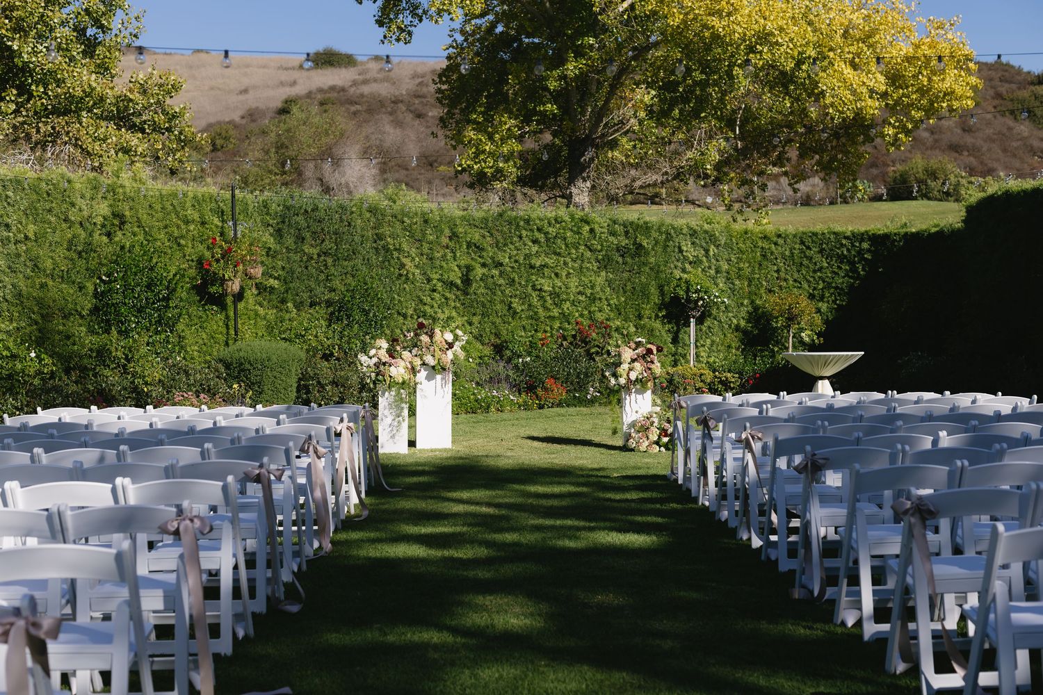 Outdoor wedding ceremony setup with white chairs arranged in rows on a green lawn.