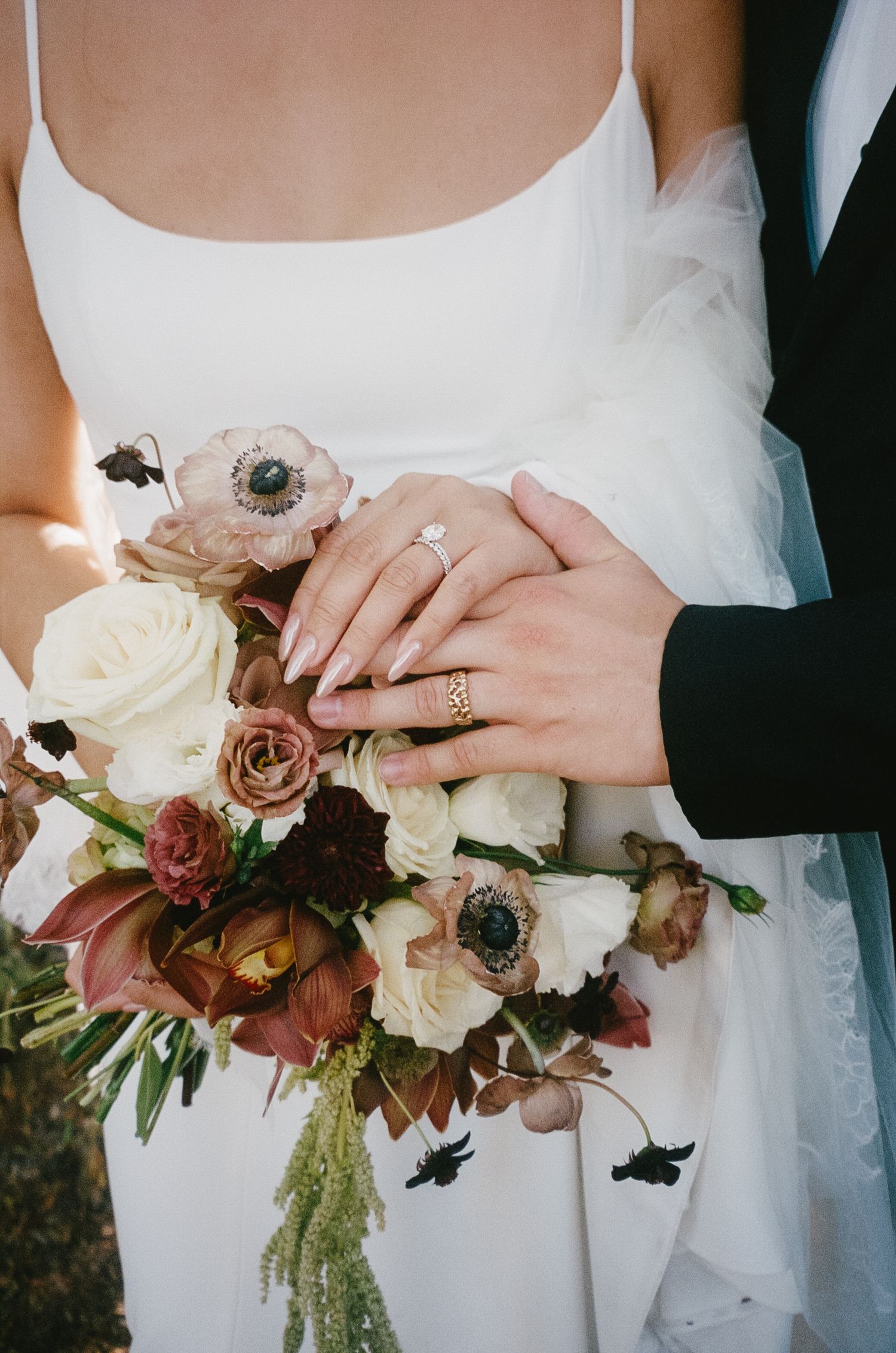 Close-up of bride and groom's hands holding elegant autumn-toned wedding bouquet with white and mauve flowers.