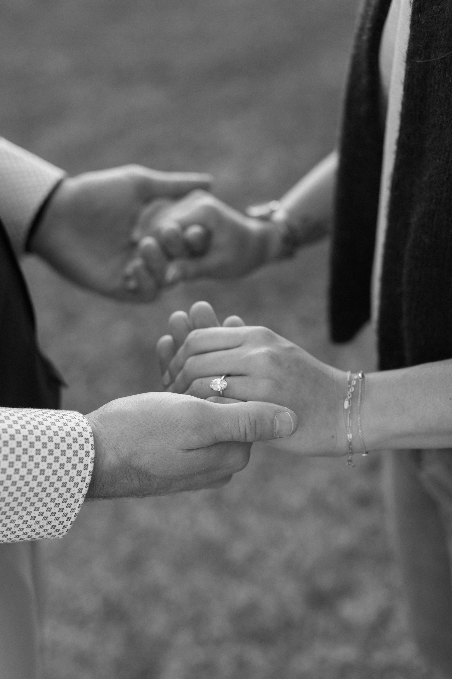 Close-up black and white photo of hands exchanging a ring during a proposal moment.