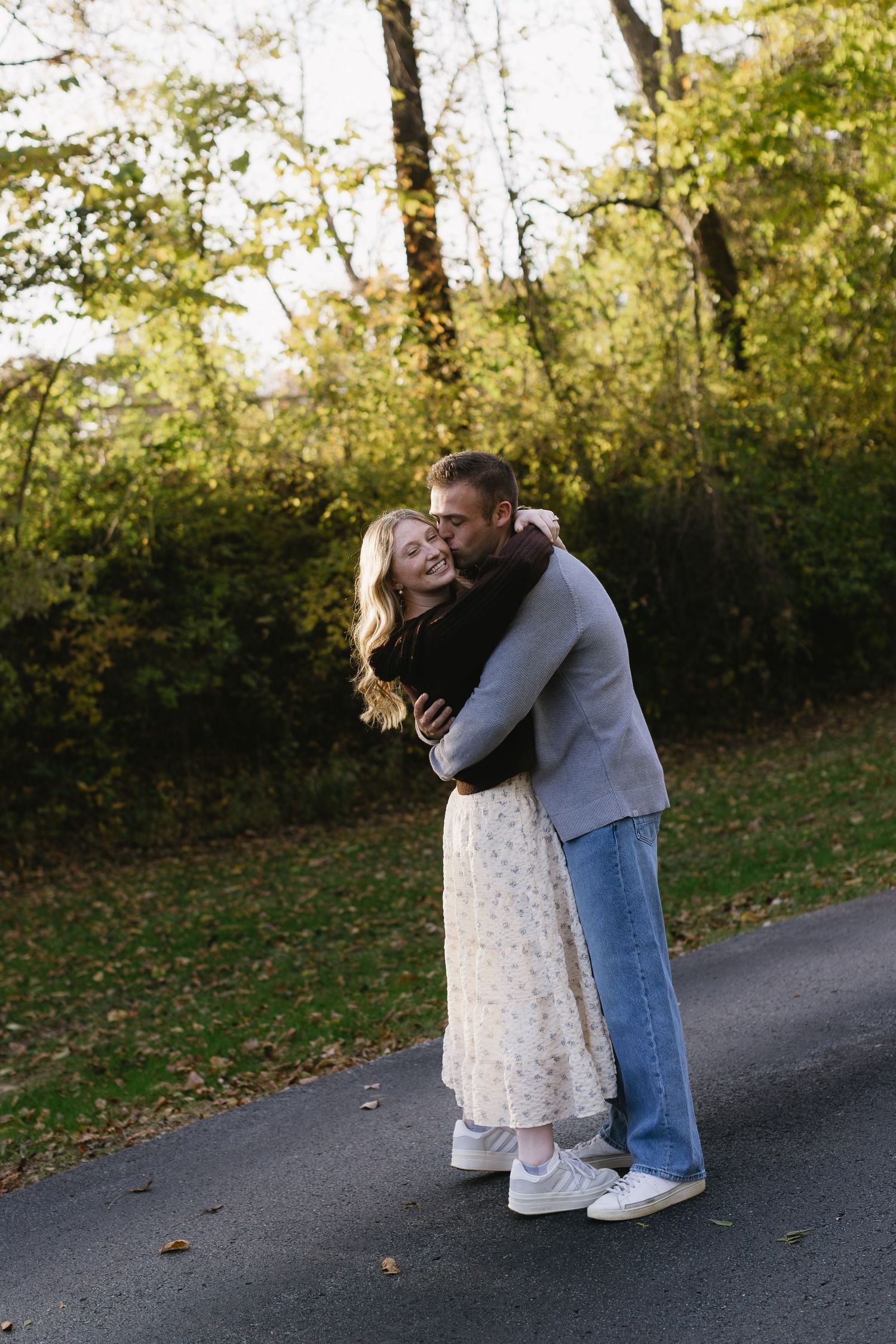Romantic autumn photoshoot on a tree-lined path with golden leaves.