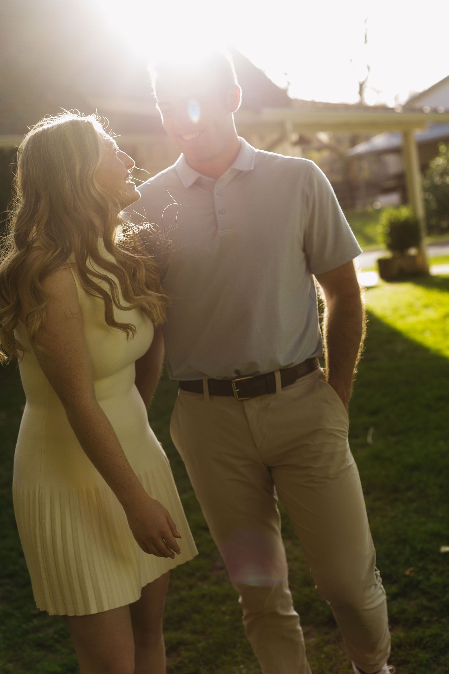 A couple poses together in golden sunlight wearing white and khaki outfits.