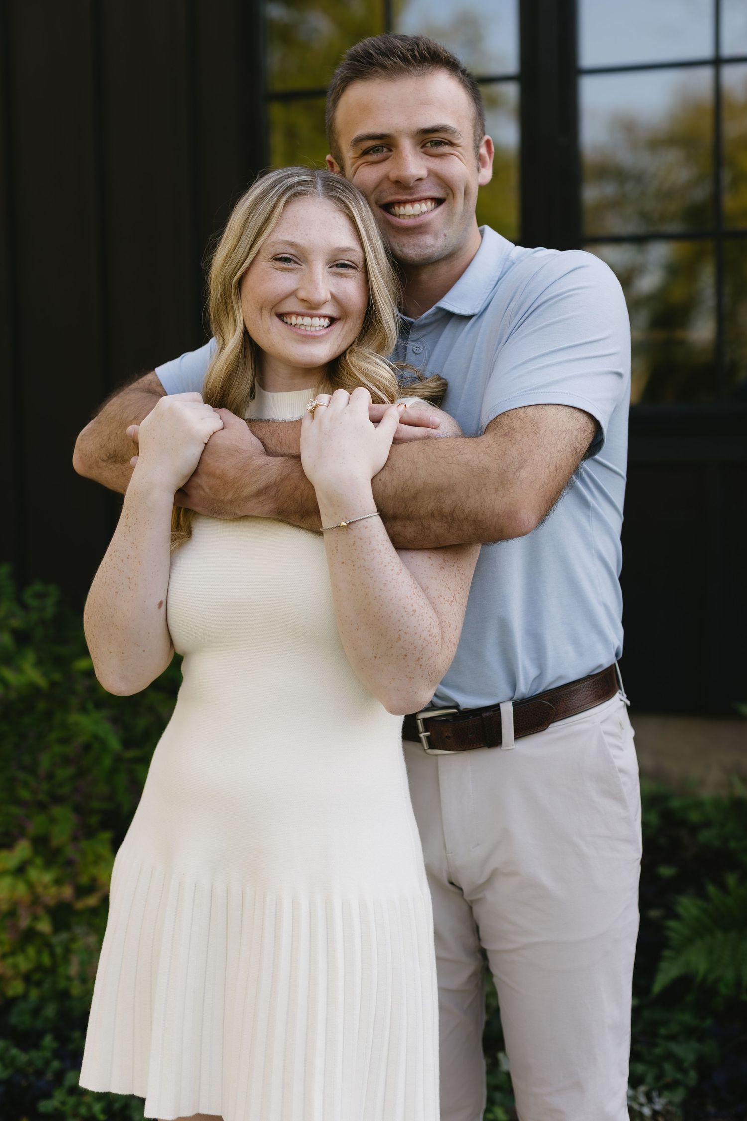 A couple poses together outdoors in coordinating white and beige outfits for a series of romantic photos.