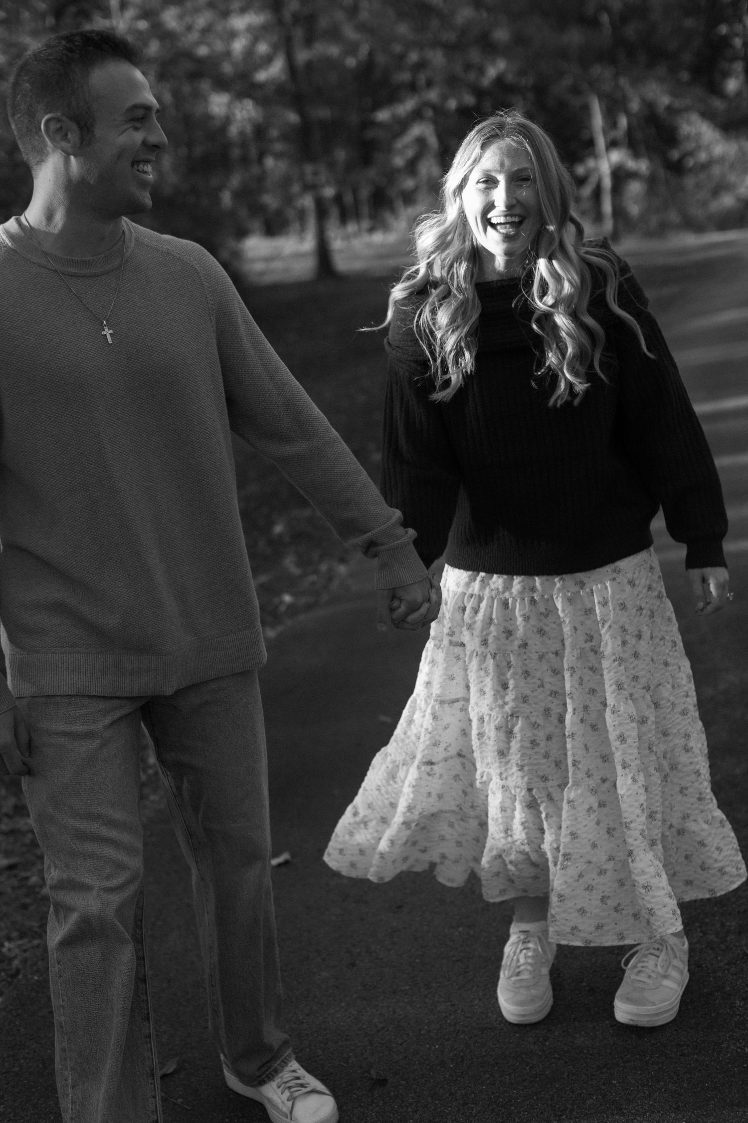 A couple sits together outdoors in casual clothing with a floral skirt against a natural background.