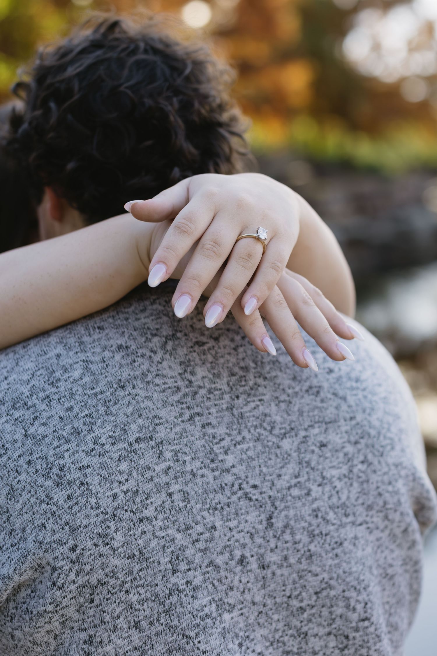 Close-up shot of hands with engagement ring resting on a gray sweater.
