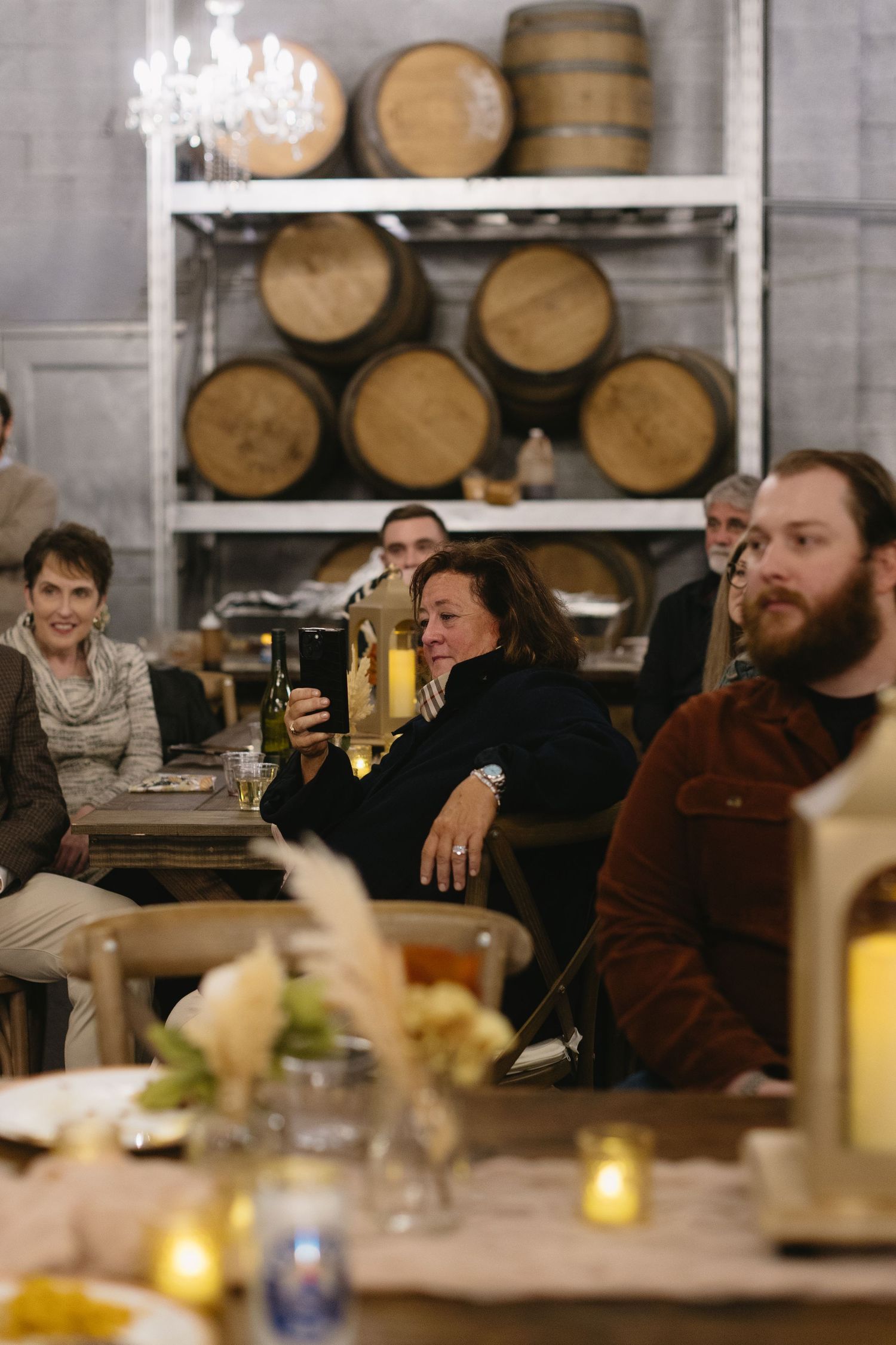 Group gathered at a table in a rustic venue with wine barrels displayed on shelves in background.