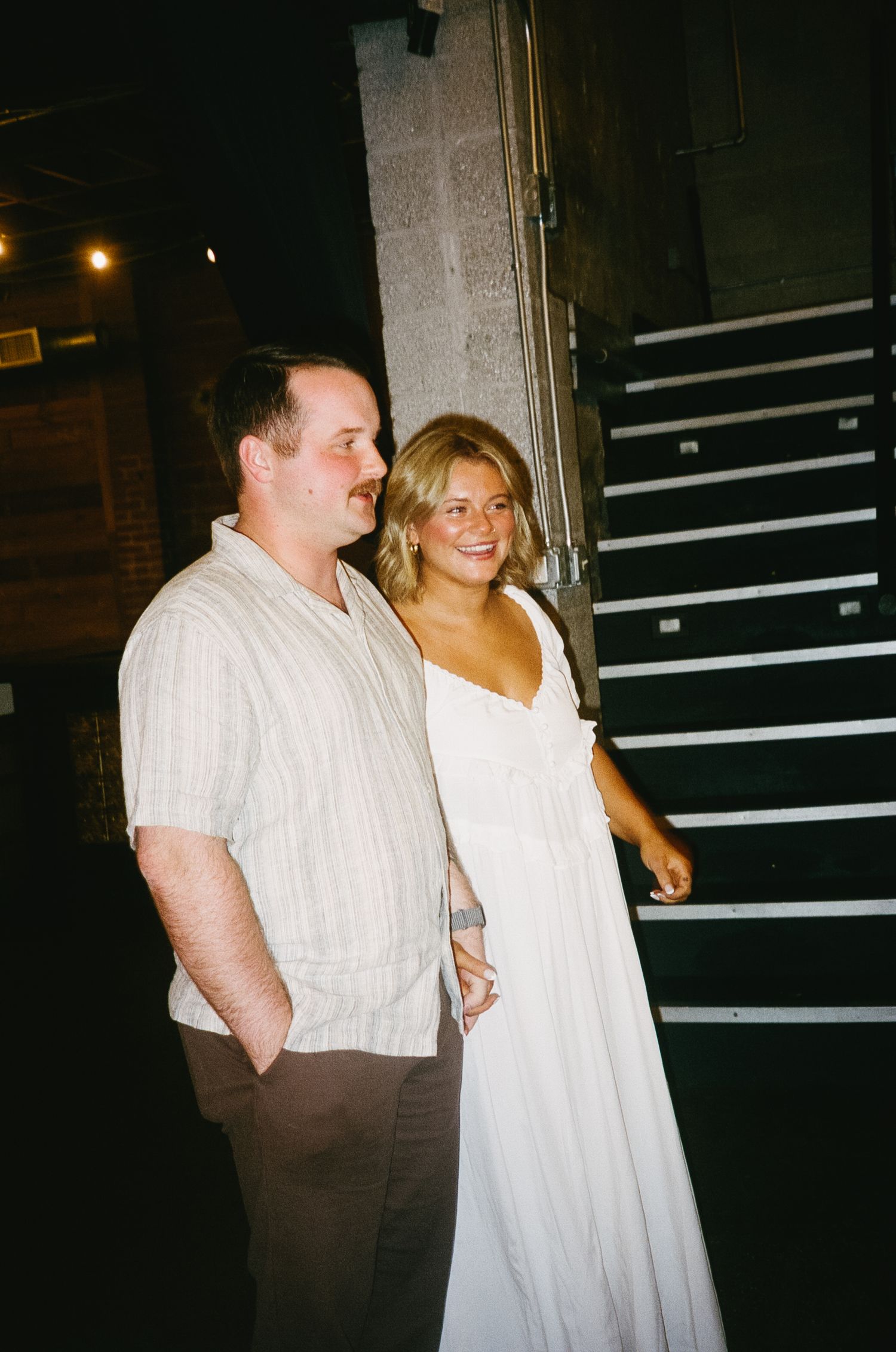Couple posing near staircase in casual wedding attire.