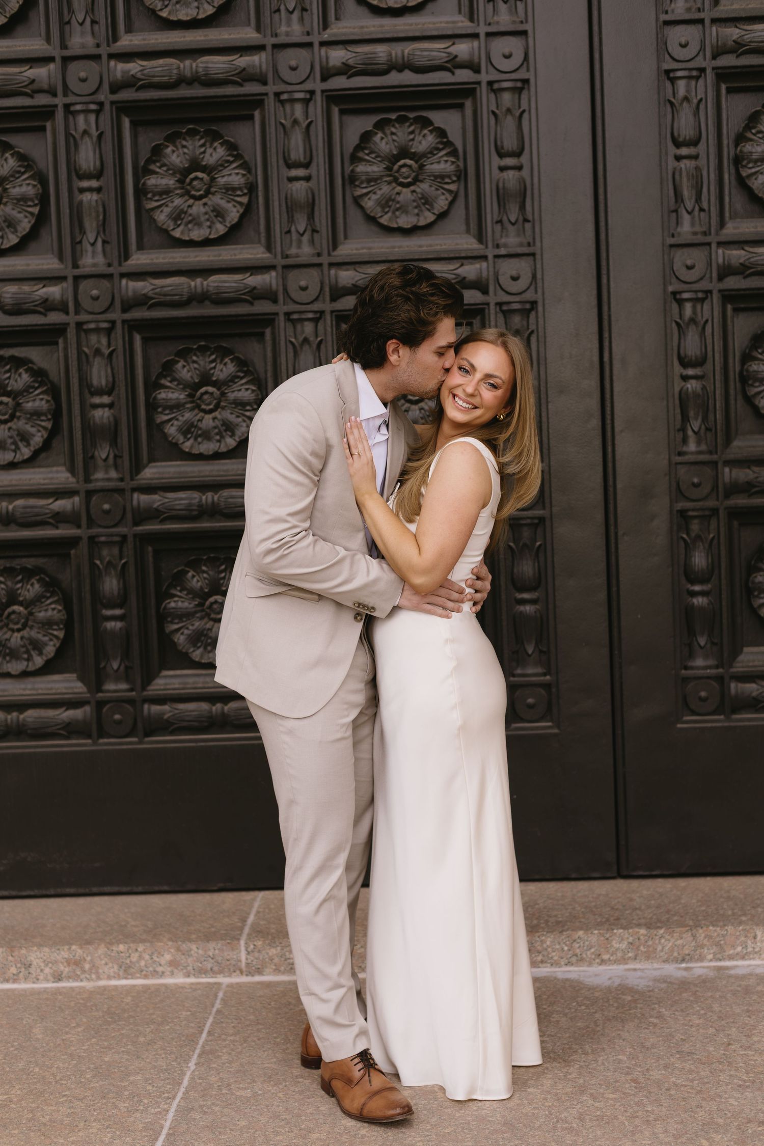 A couple sharing an intimate moment against an ornate black door background.