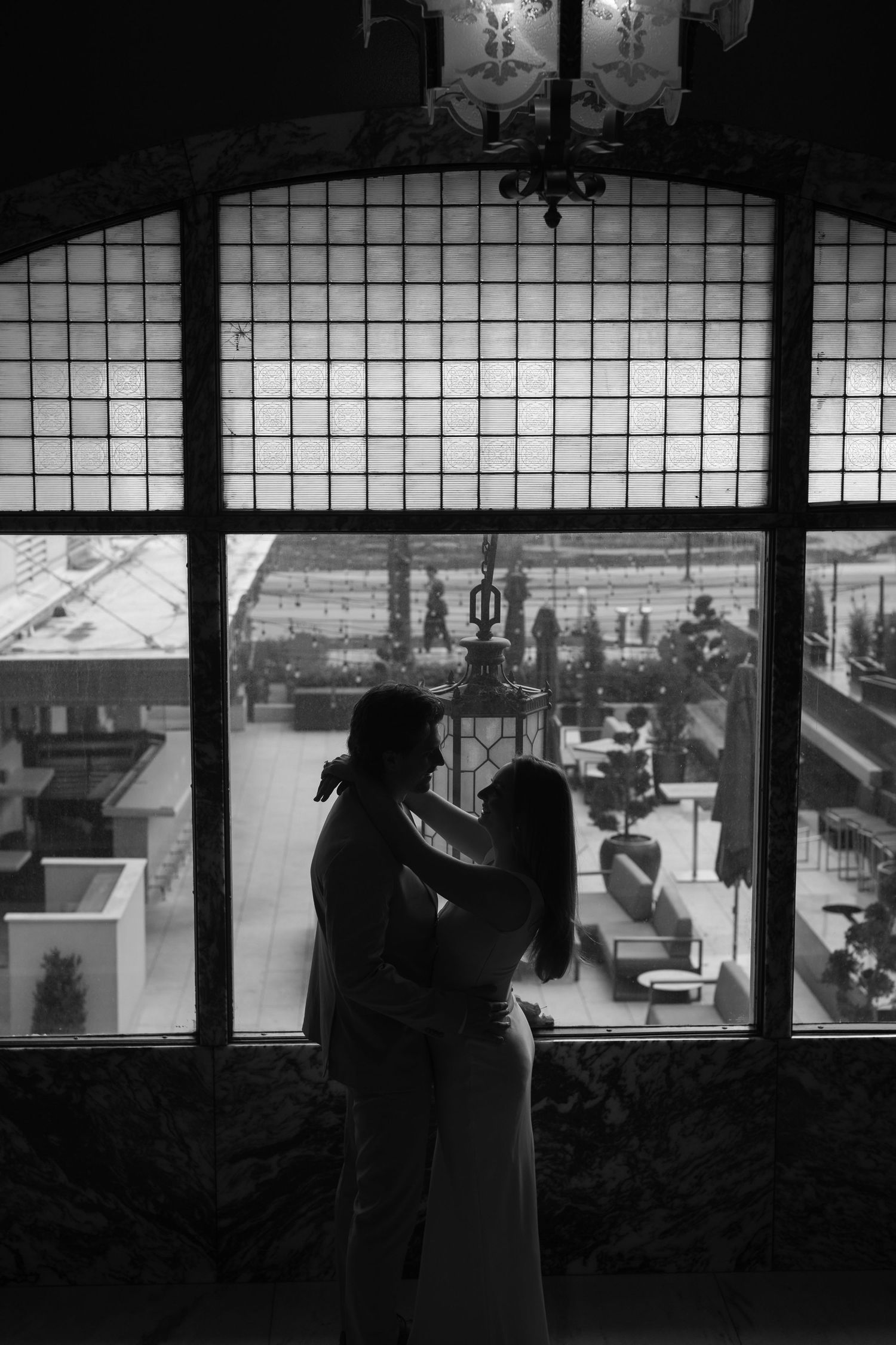 Silhouettes of a couple stand against large windows with a cityscape view.