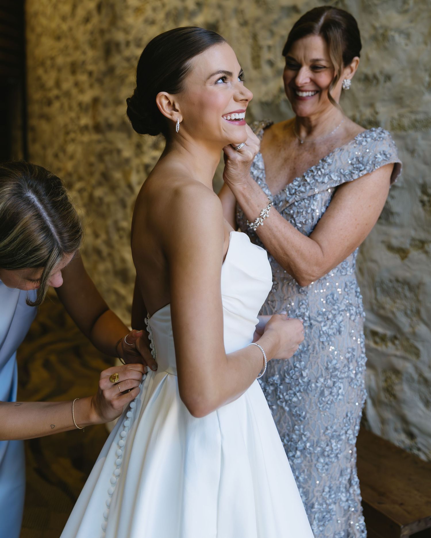 Emotional getting ready moment with two ladies in white and silver dresses preparing for a special occasion.