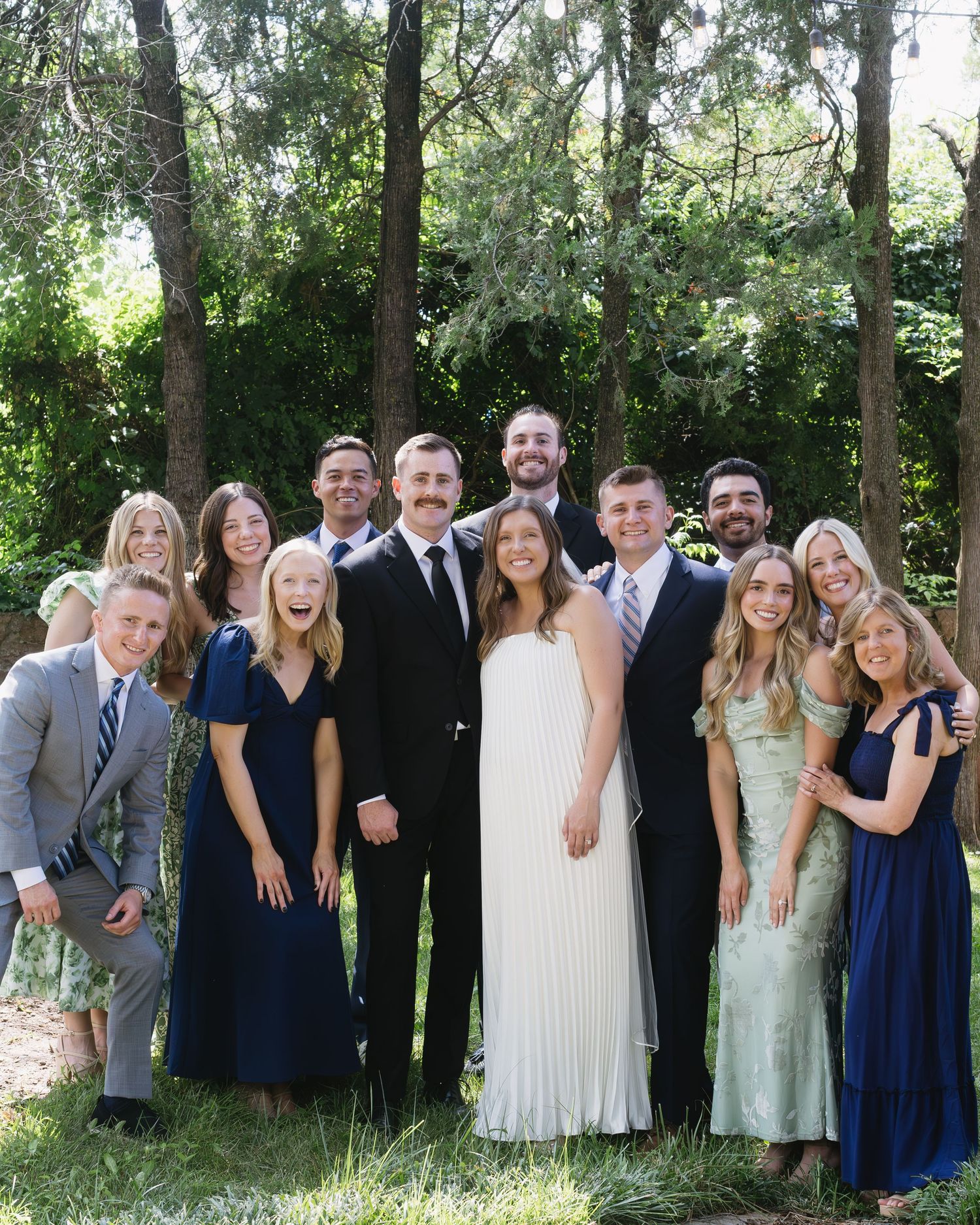A wedding party poses outdoors in navy and mint green dresses with a bride in white.