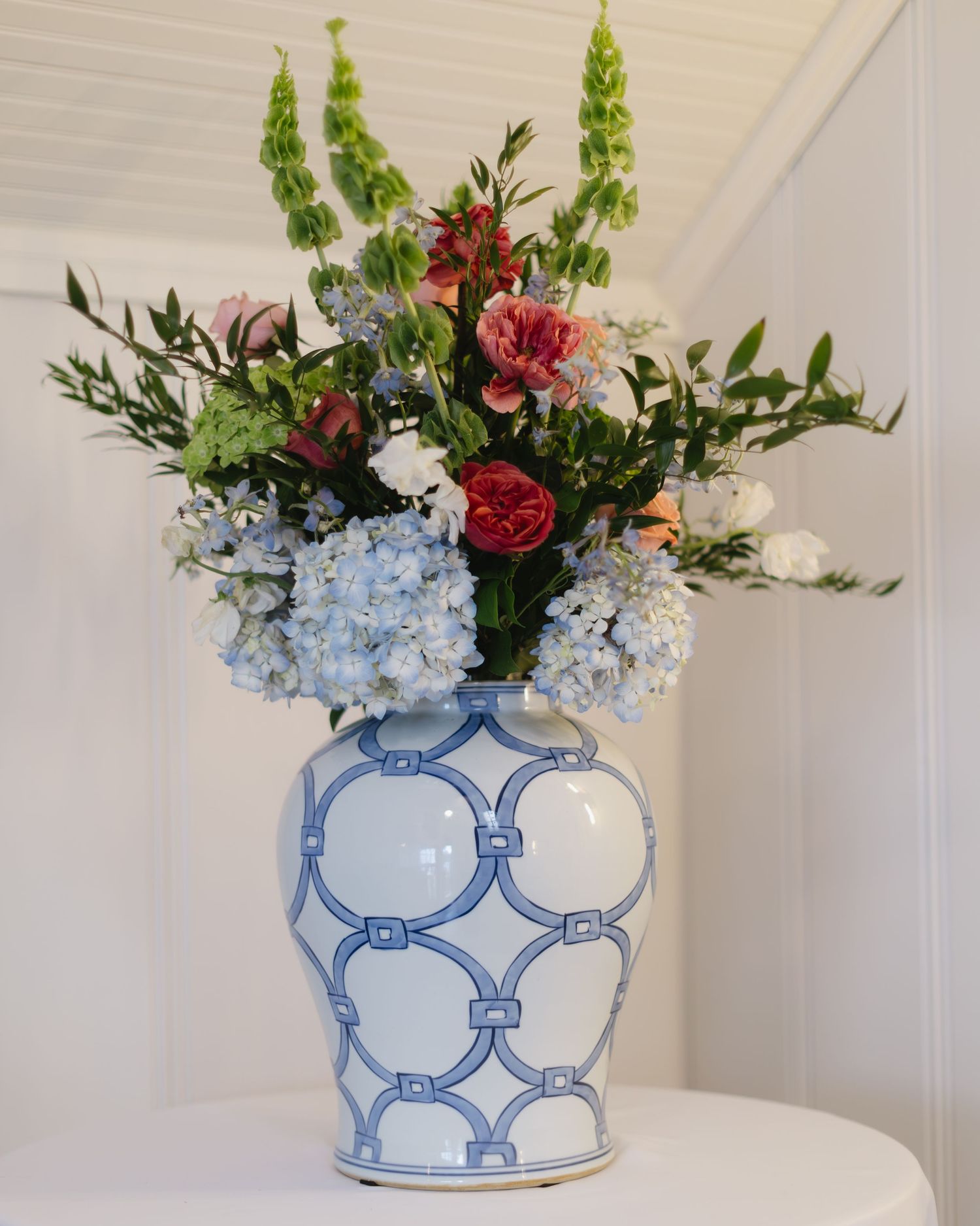 Blue and white chinoiserie vase filled with hydrangeas and red roses on a white shelf.