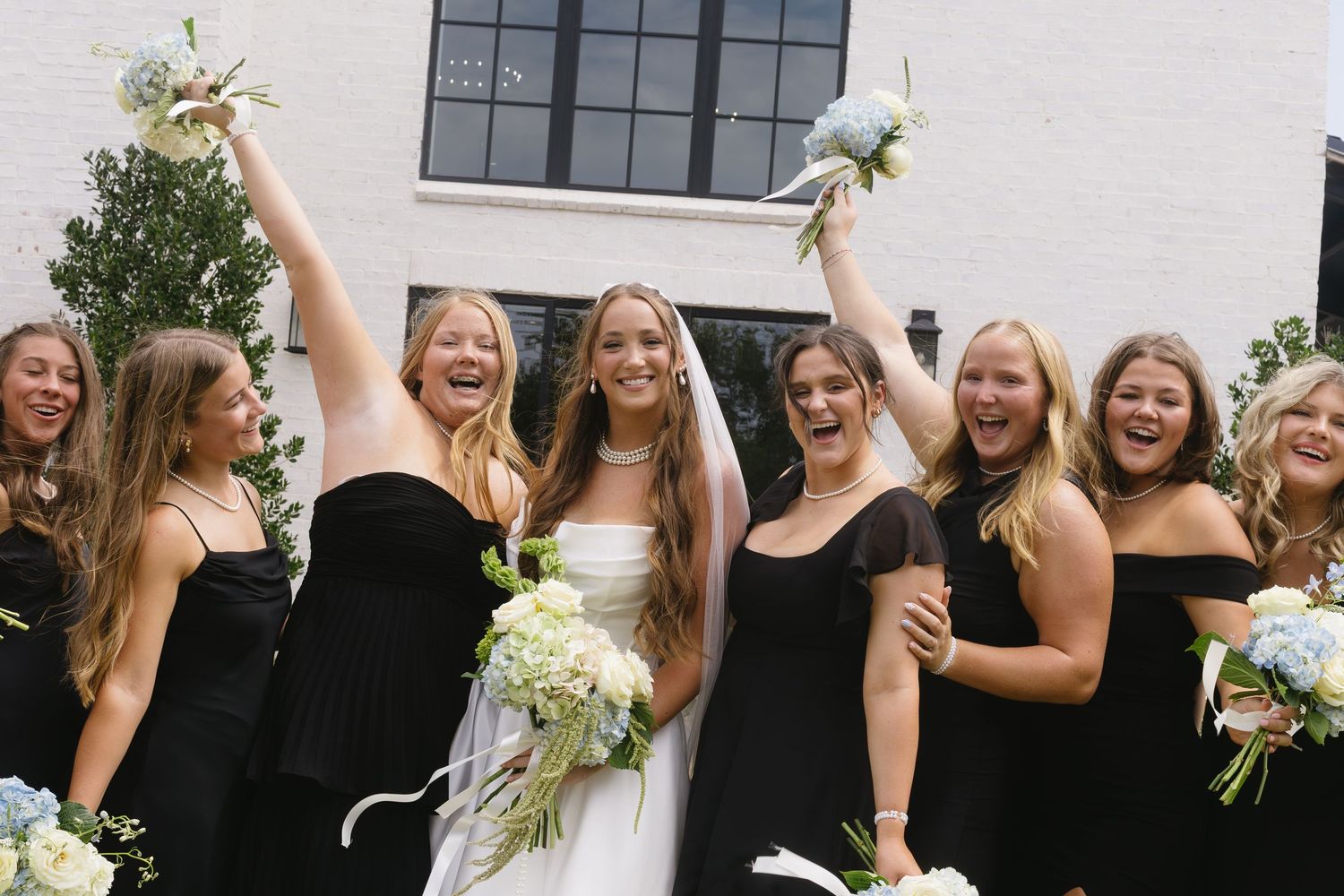 Wedding party in coordinated black dresses celebrating outdoors with joyful expressions.
