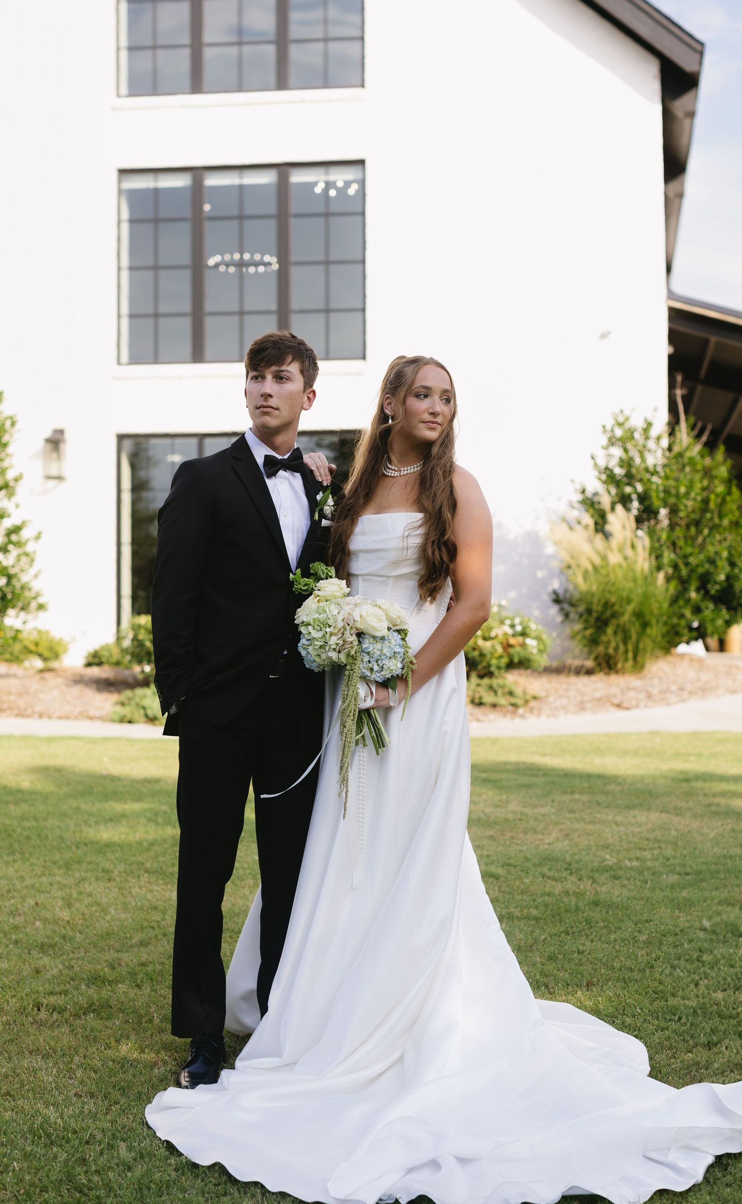 Outdoor wedding photos taken in front of a modern white building with large windows.
