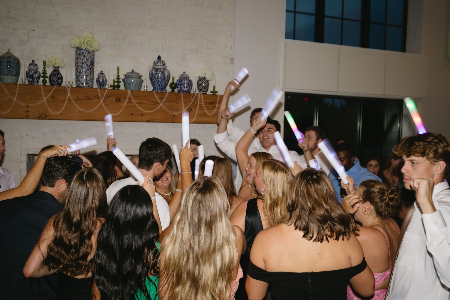 Wedding reception party with guests raising hands and dancing under indoor lighting.