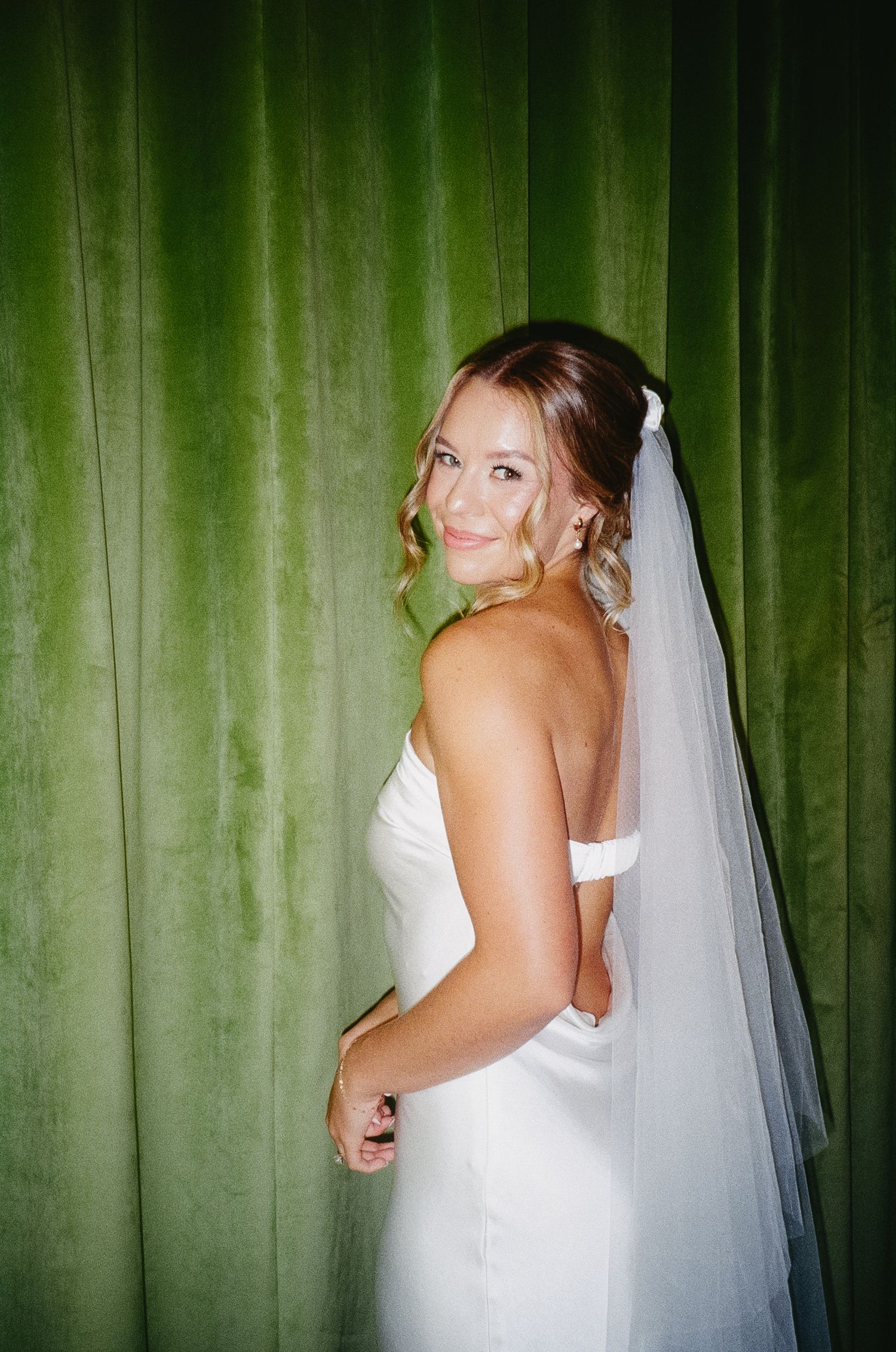 Wedding dress portraits against a green velvet curtain backdrop showing details of a strapless white gown.