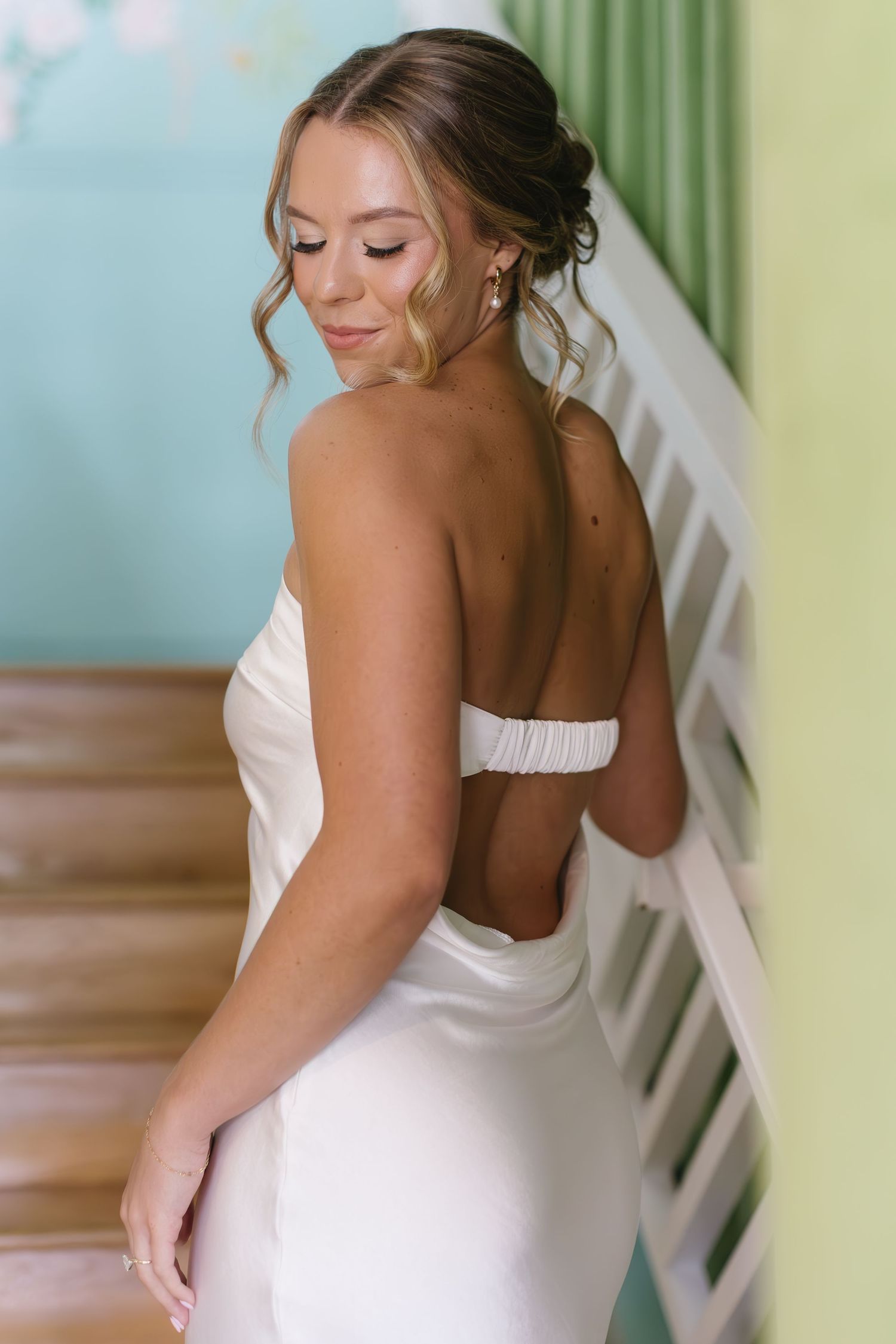 Close-up view of a white wedding dress with delicate details shown from the back against a green wall backdrop.