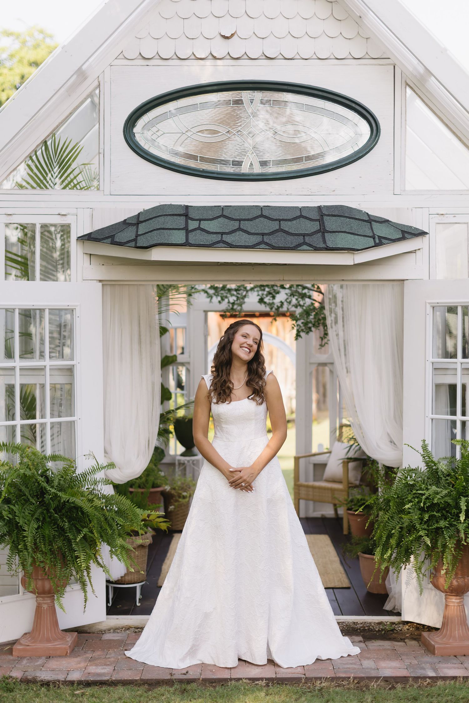 A white gazebo with decorative trim and hanging plants serves as an elegant bridal backdrop.