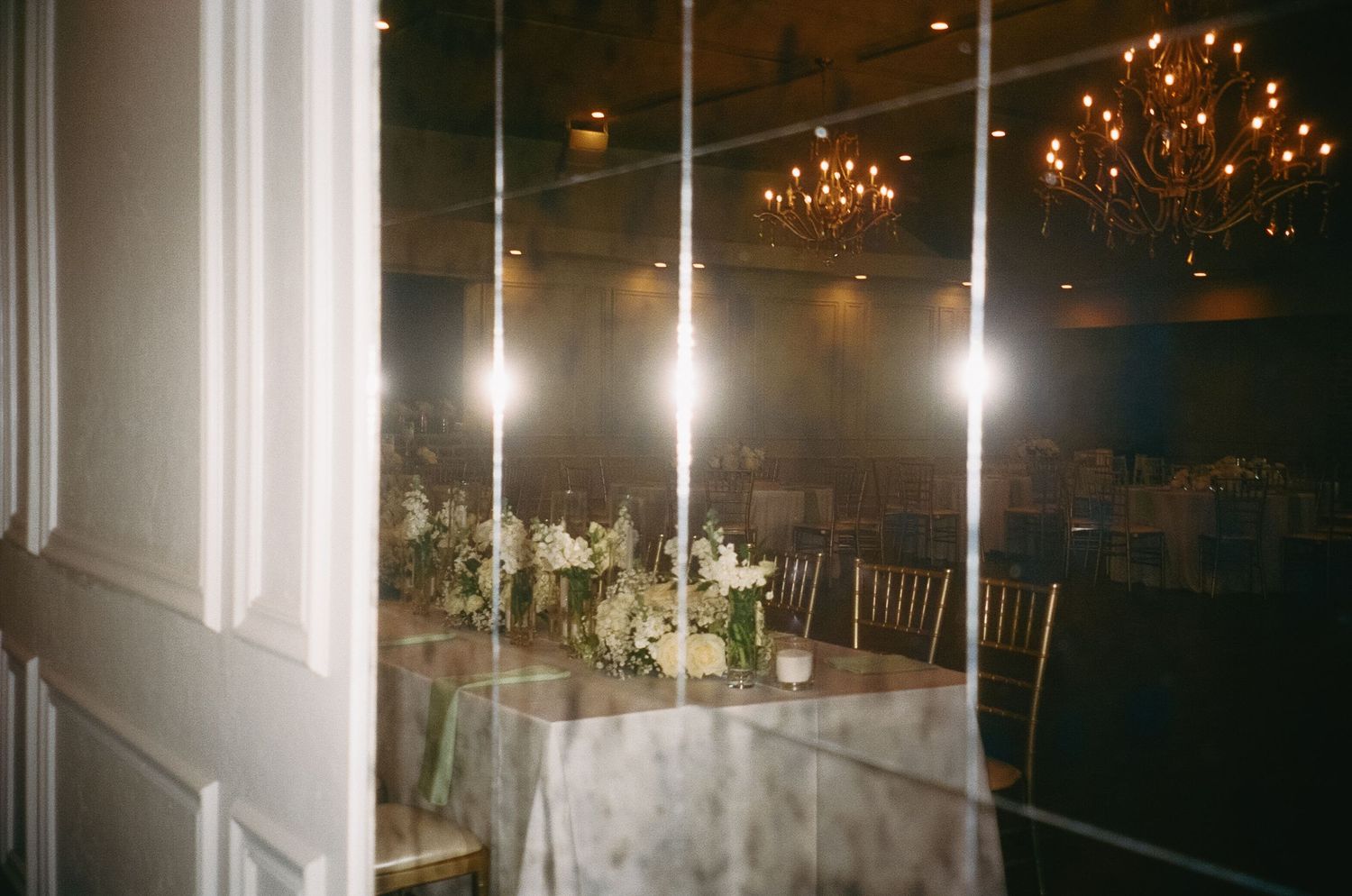 A grand wedding reception hall with crystal chandeliers and elegant white decor glowing in warm lighting.
