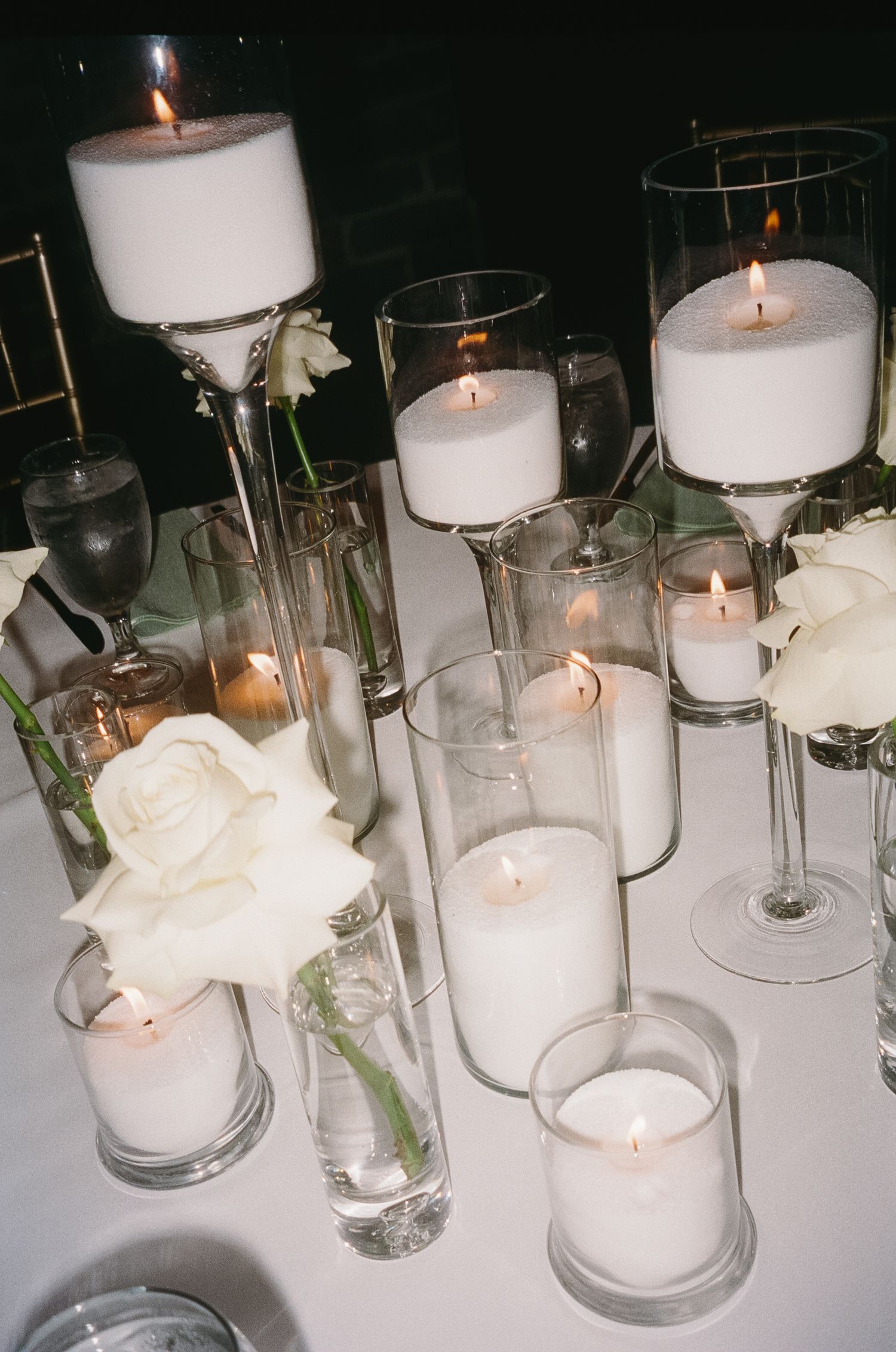 White pillar candles and roses create an elegant table centerpiece with glass cylinder vases in modern wedding decor.