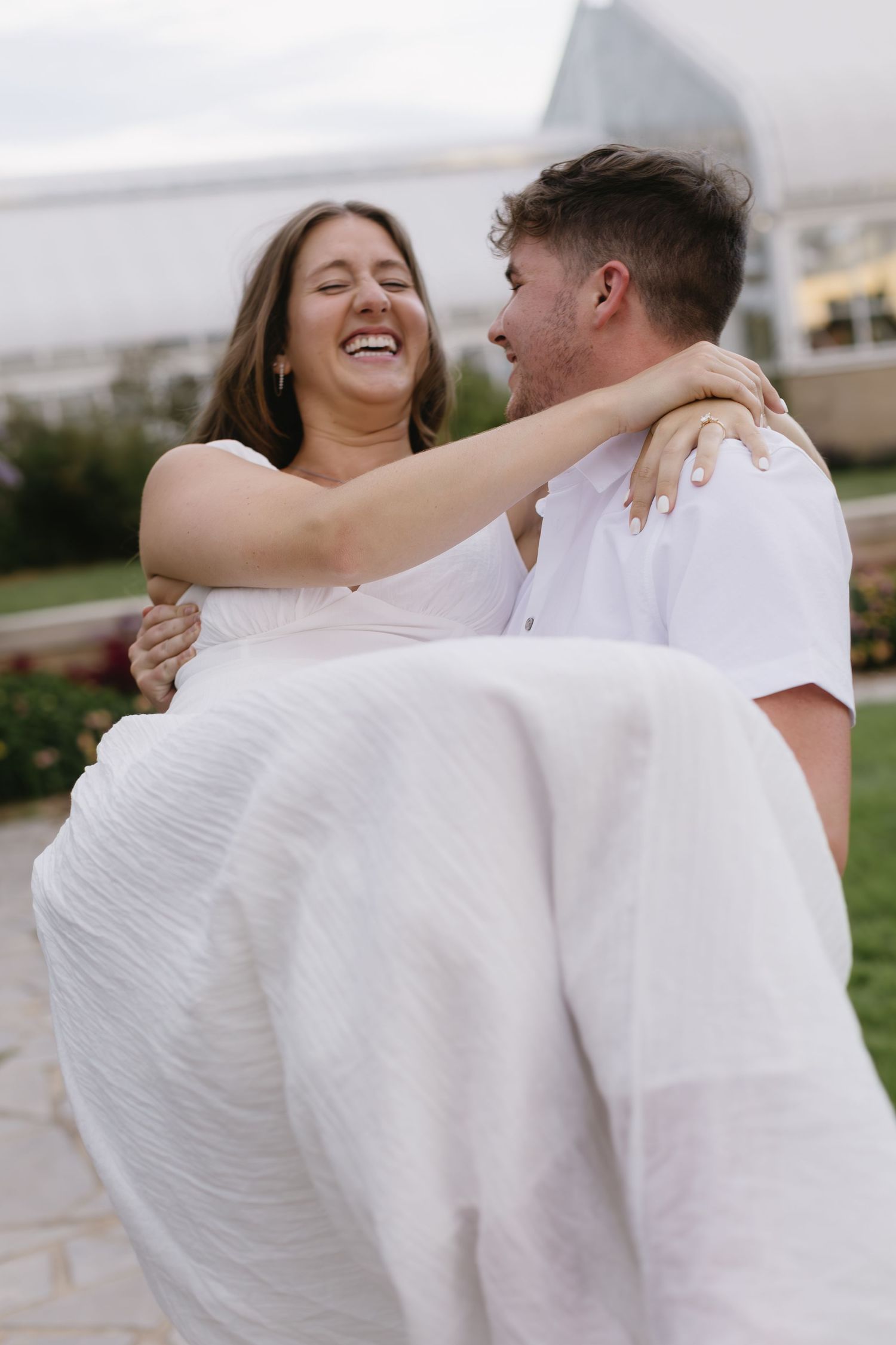 A couple in white clothing spins and dances together outdoors with pure joy on their faces.