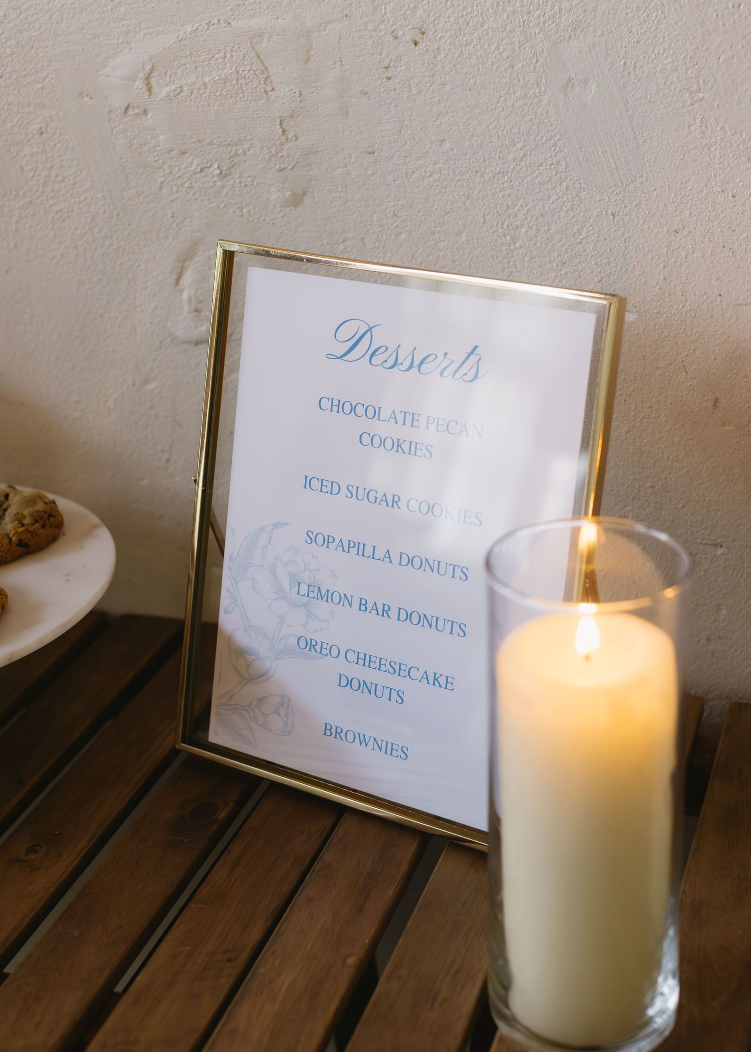 A dessert menu display with candles showing items like cookies and brownies in elegant blue script.