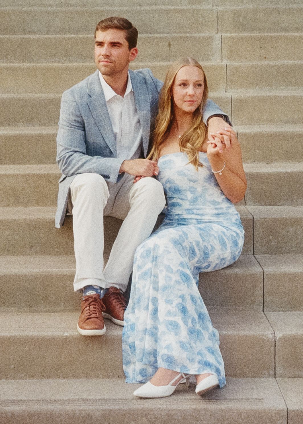Couple sitting on concrete steps wearing coordinated blue and white outfits in a romantic outdoor setting.