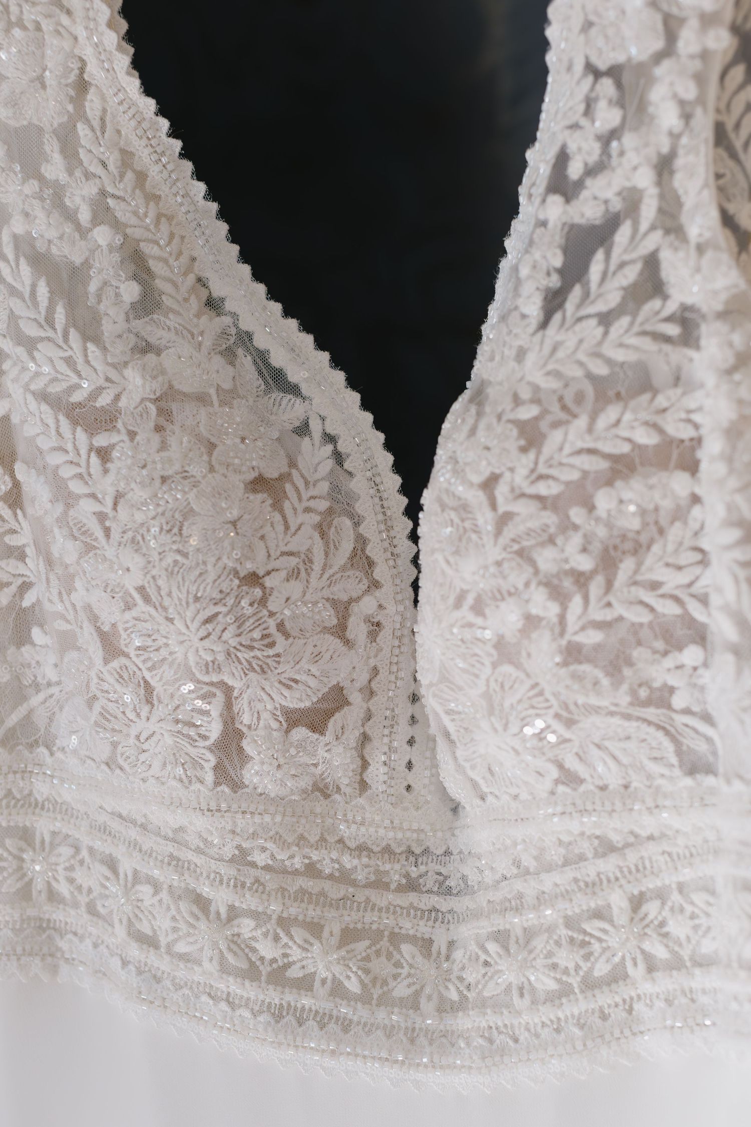 Intricate white lace detail with delicate floral patterns and scalloped edges on a wedding dress bodice.